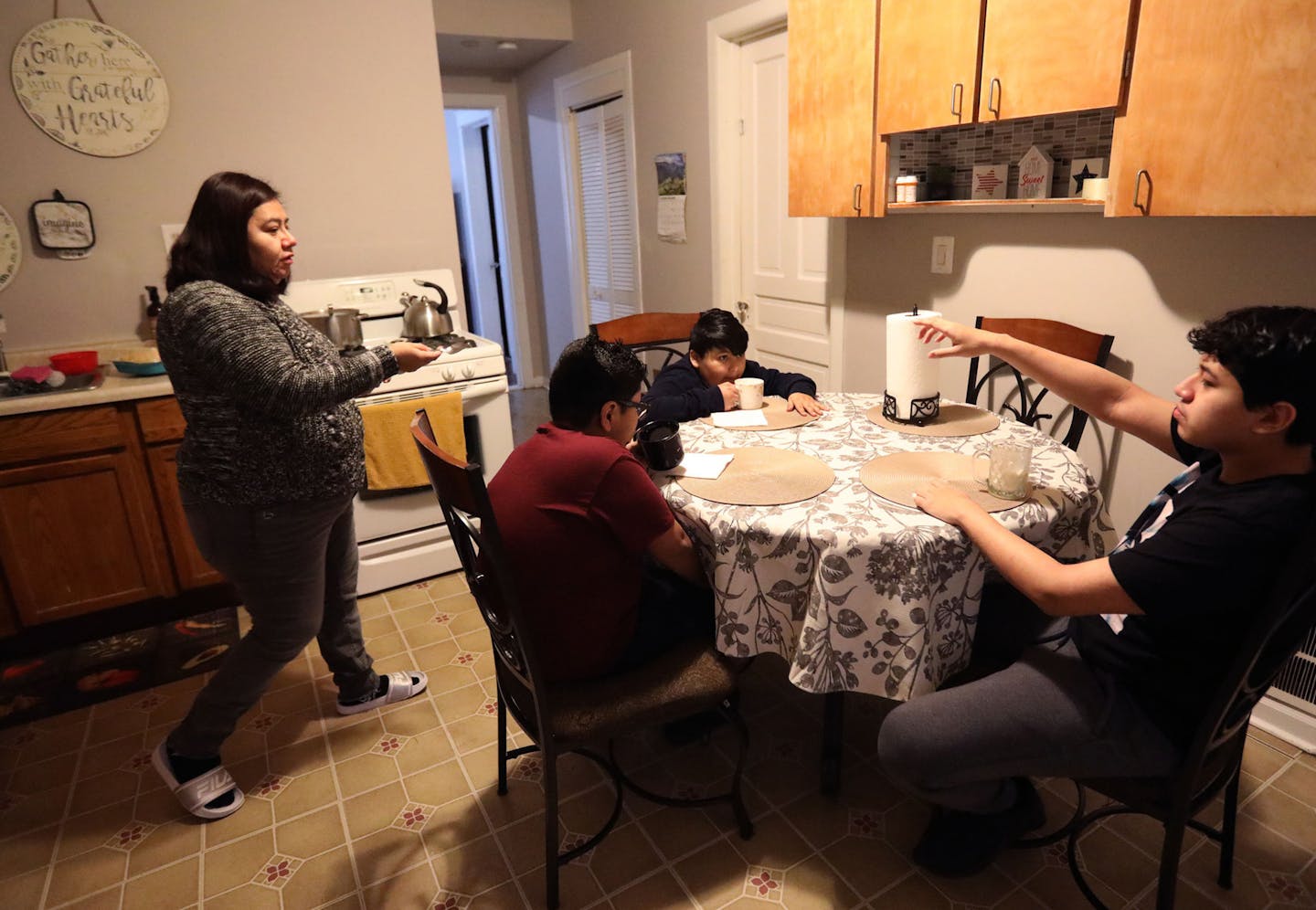 Rosa Valladares, left, brings a spoon to her son Angel, far right, as Junior, center, and Emilio, second from right, get ready for school at the Reyes apartment in Chicago on Tuesday, Nov. 23, 2021. (Antonio Perez/Chicago Tribune/TNS)