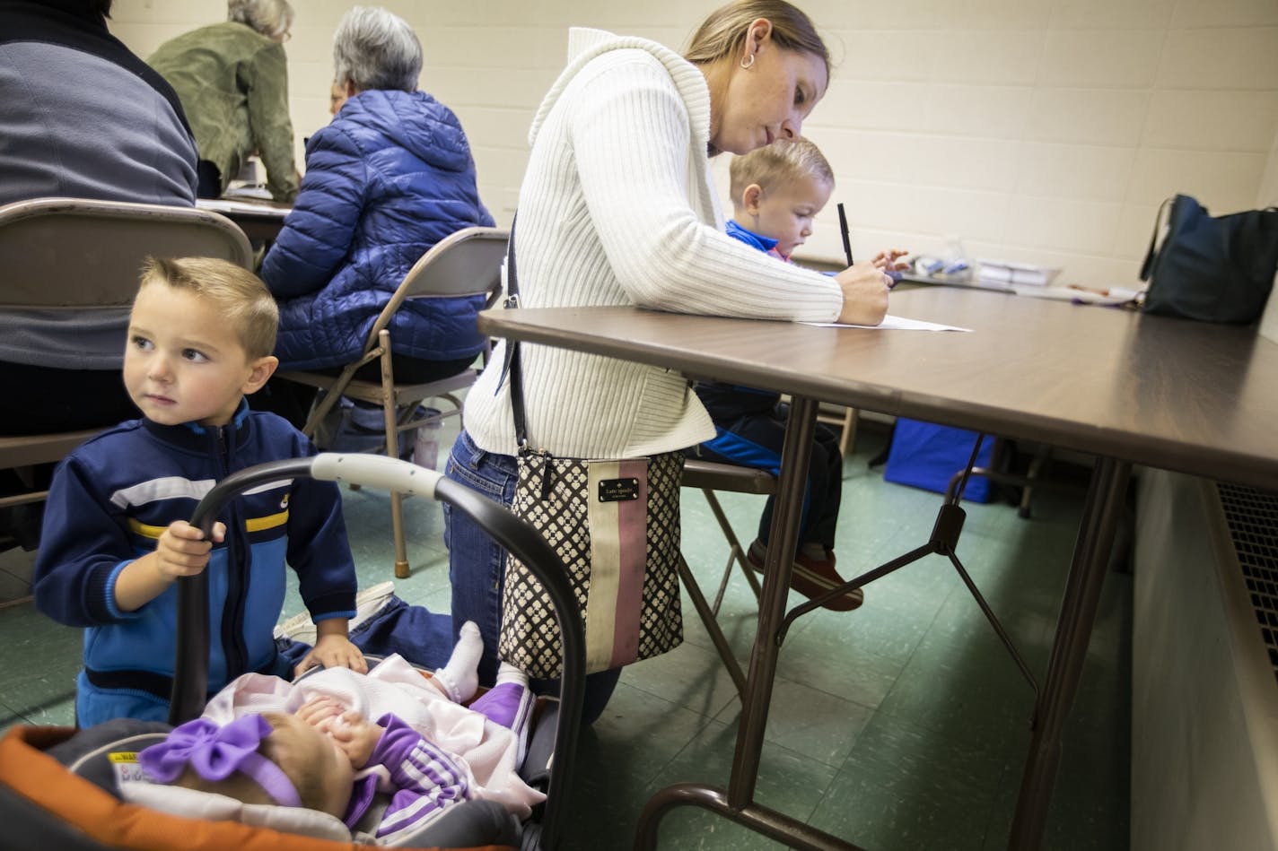 Mary Menne, with her children Peter, from left, 4, Josephine, five months, and Isaac, 2, fills out her ballot at St. Joseph's Catholic Church Parish Center in Henderson.