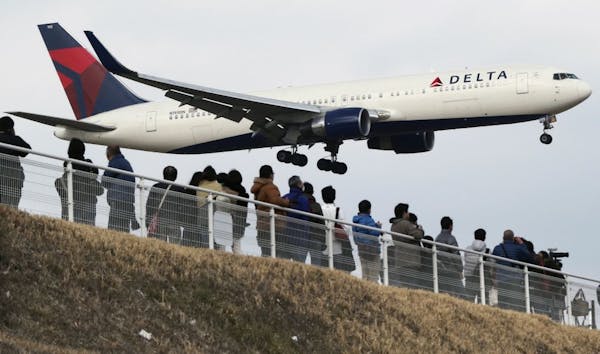 In this March 14, 2015, file photo, people watch a landing Delta Air Lines jet approach the Narita International Airport from a popular viewing spot a