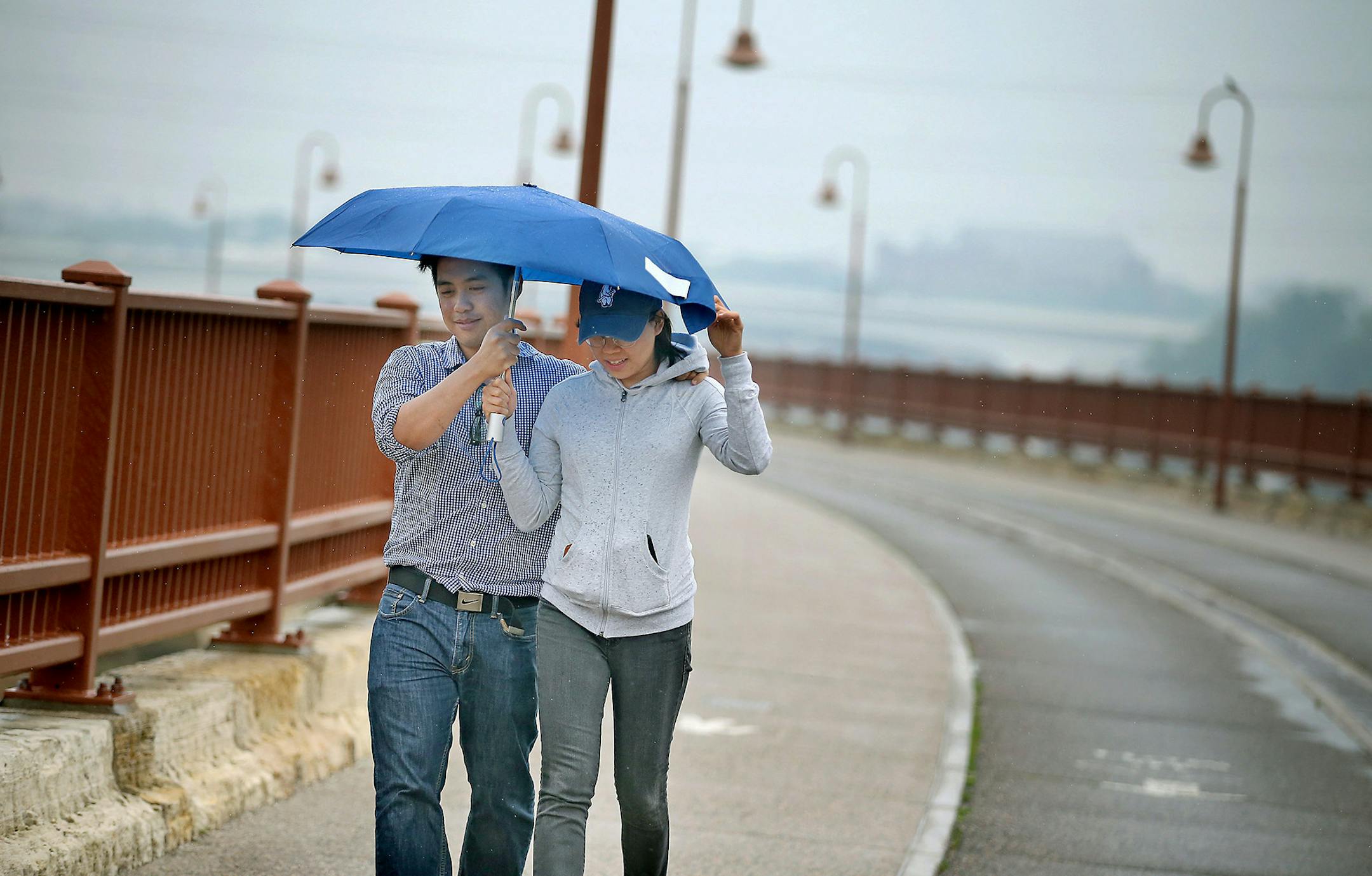 Frenz and Jade Cabagnot of Chicago, shared an umbrella as they made their way across the Stone Arch bridge on a rainy Monday, July 6, 2015 in Minneapolis, MN. ] (ELIZABETH FLORES/STAR TRIBUNE) ELIZABETH FLORES • eflores@startribune.com