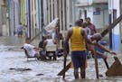 In this Sunday, Sept. 10, 2017 photo released by Granma, men play dominoes in the middle of a flooded street as others pull broken furniture from calf