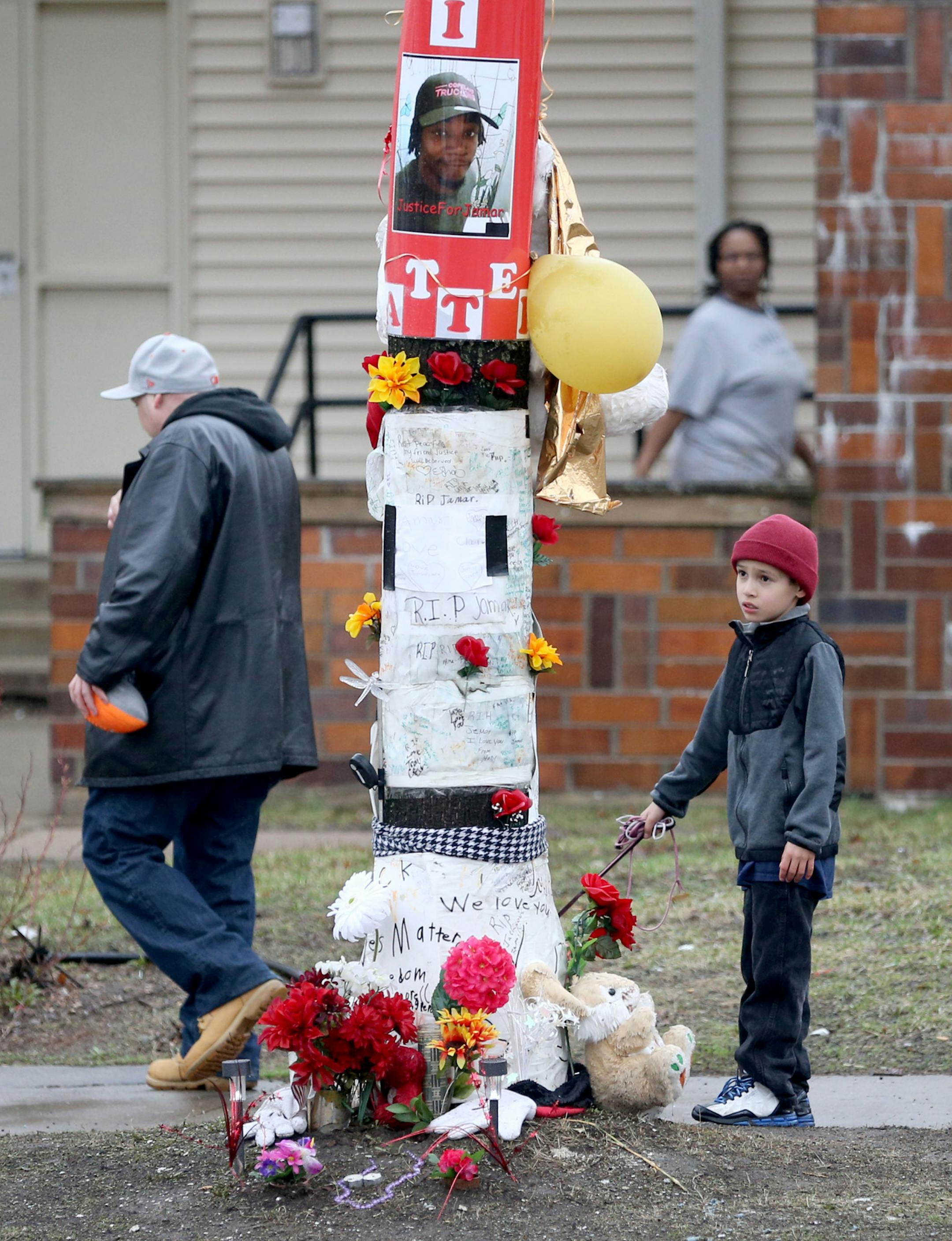People walk by a memorial to Jamar Clark in the 1600 block of Plymouth Ave. N. Wednesday, March 30, 2016, in Minneapolis, where Clark was shot in November 2015. Pausing to look at the memorial is Daren Chamberlain, 8, with his dog Lucey, as his father Dagan Chamberlain walks by. Hennepin County Attorney Mike Freeman on Wednesday announced his decision not to charge Officers Mark Ringgenberg and Dustin Schwarze in the shooting of 24-year-old Jamar Clark. (David Joles/The Star Tribune via AP) MAND