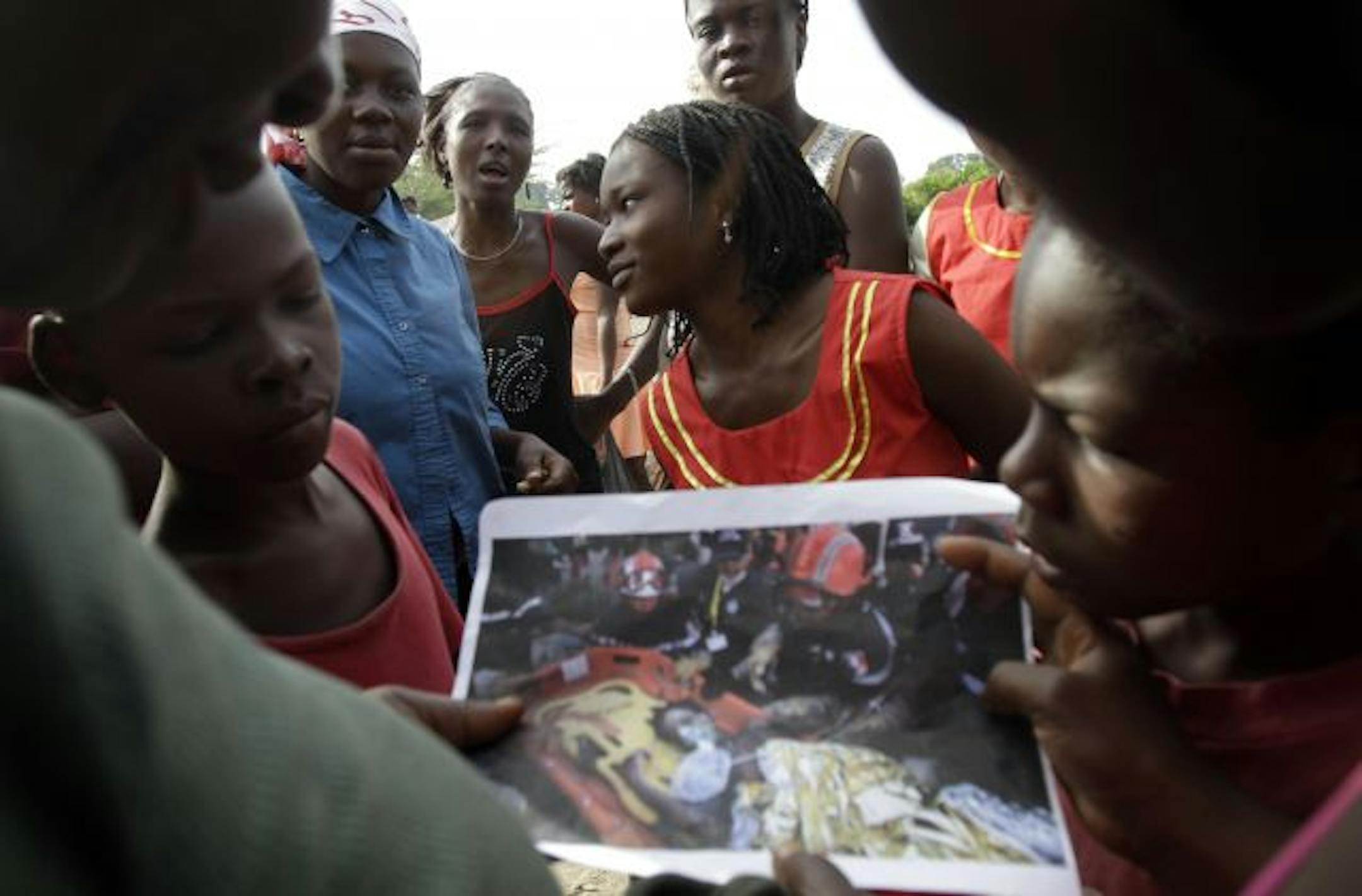Earthquake survivor Darlene Etienne, center, showed a photo of her rescue taken by Associated Press photographer Ramon Espinosa to neighbors in Marchand Dessaline, Haiti, on Sunday. The 17-year-old was pulled from the rubble in Port-au-Prince more than two weeks after the Jan. 12 quake last year
