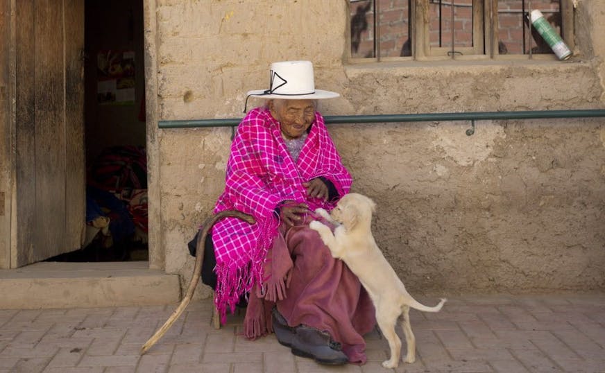 In this Aug. 23, 2018 photo, 117-year-old Julia Flores Colque plays with "Chiquita," one of the family pet dogs, while sitting outside her home in Sacaba, Bolivia. Flores Colque, who never married or had children, enjoys the company of her dogs, cats and rooster.