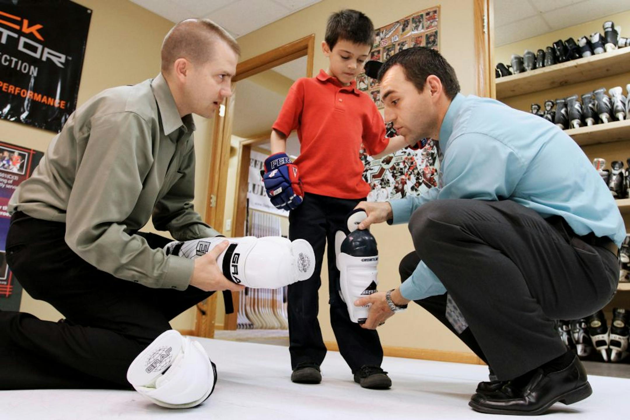 Shane Hudella, left, and Milan Tomaska fit Tomaska's son Milan with new shin guards. The Tomaskas visited Defending the Blue Line in Hastings to trade some hockey gear that Milan had outgrown for new equipment. Defending the Blue line is owned and founded by Hudella, who grew up in Hastings.