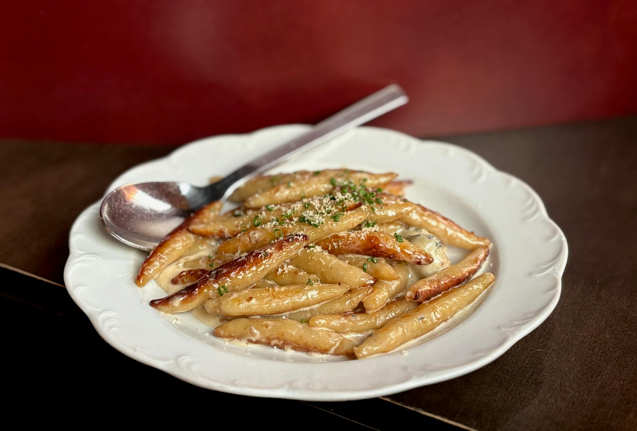 A plate of finger shaped dumplings with browed middles in a buttery sauce garnished with finely chopped chives.