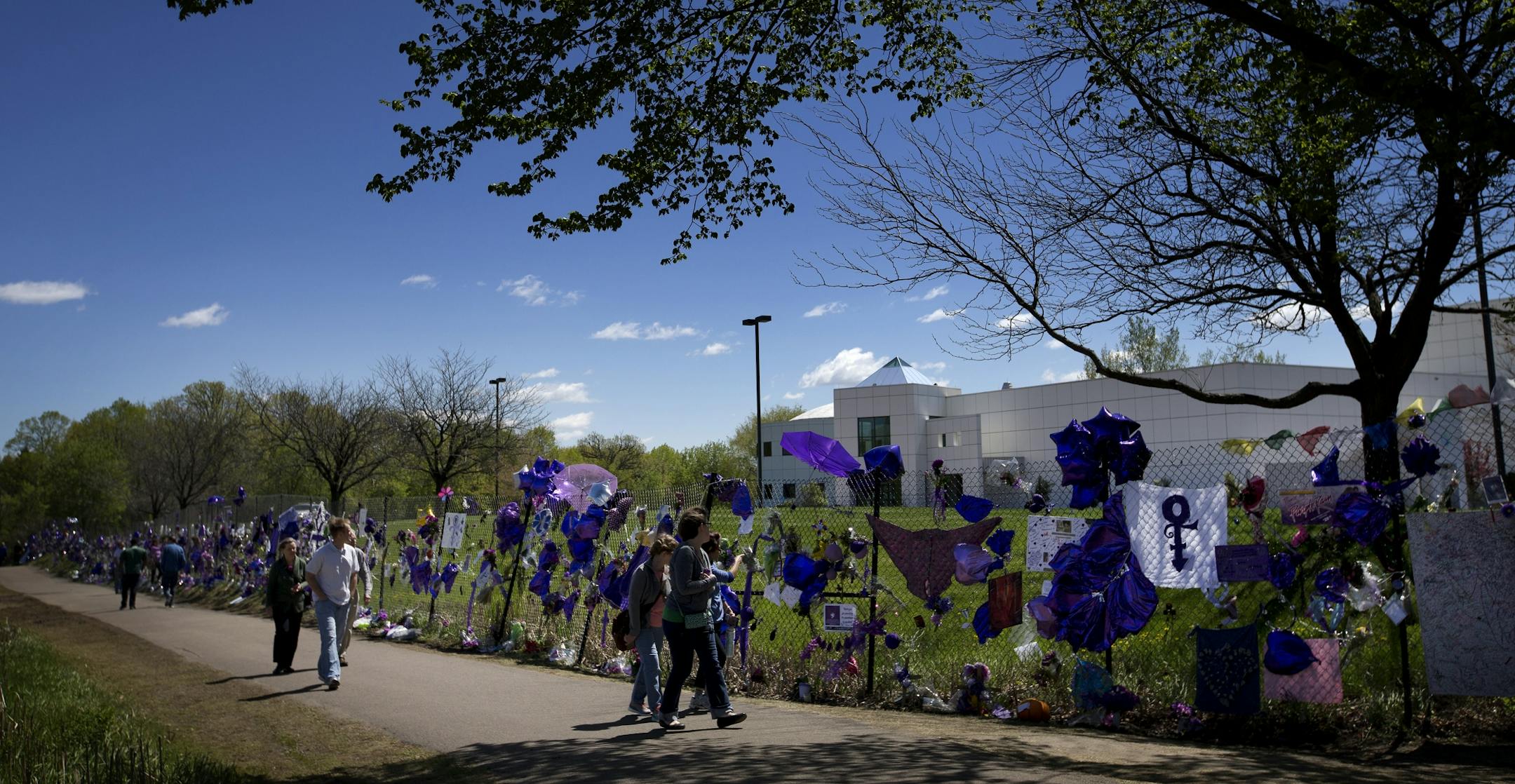 People walked by the balloons flowers and other mementos attached to the fence surrounding Paisley Park in Chanhassen, MN honoring the death of Prince.