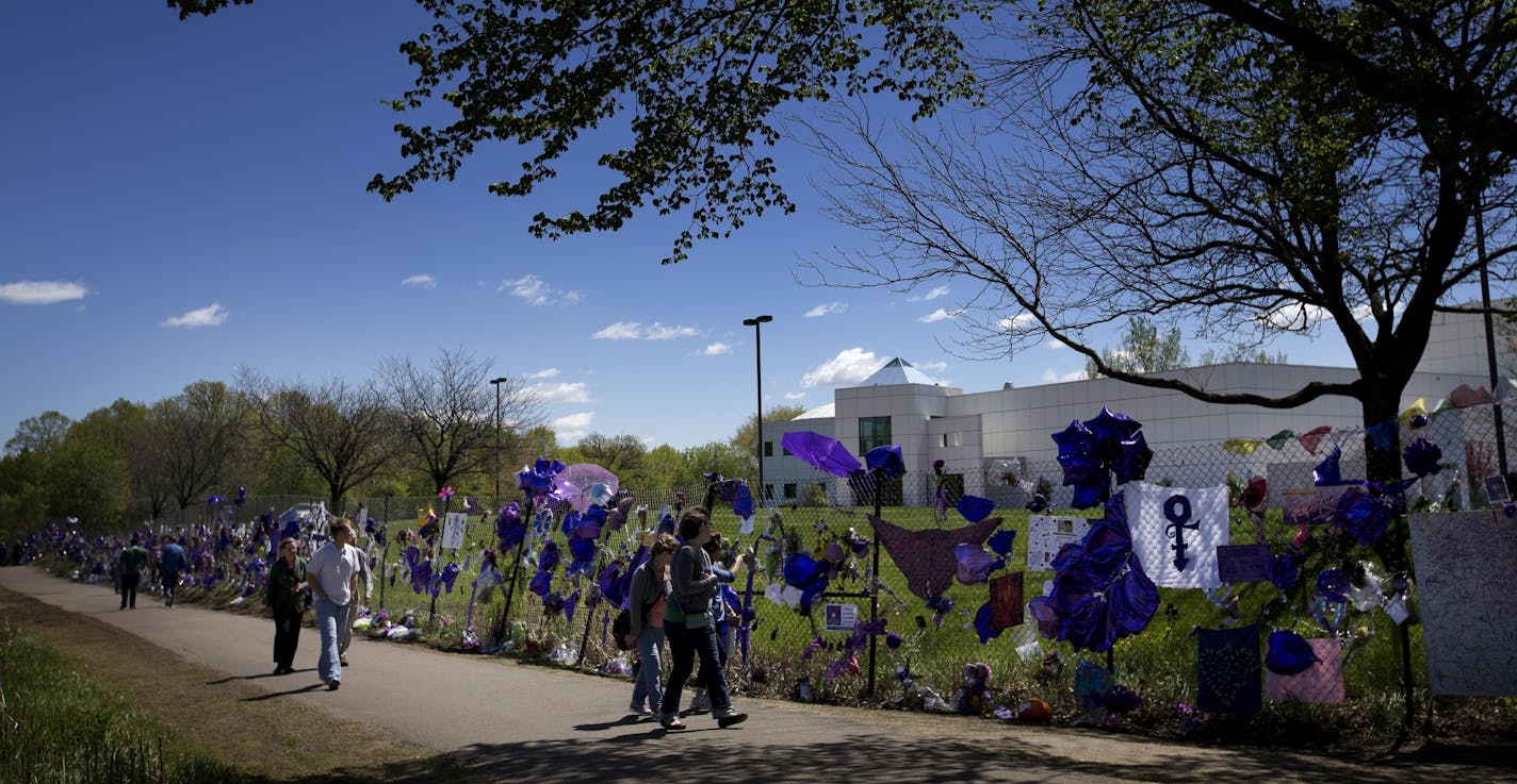 People walked by the balloons flowers and other mementos attached to the fence surrounding Paisley Park in Chanhassen, MN honoring the death of Prince.