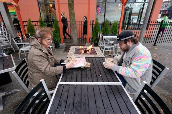Diners Bonnie Breitman, left, and Casey McGan huddle near an outdoor gas fire as they eat lunch outside in a blustery wind Tuesday, Nov. 17, 2020, in 