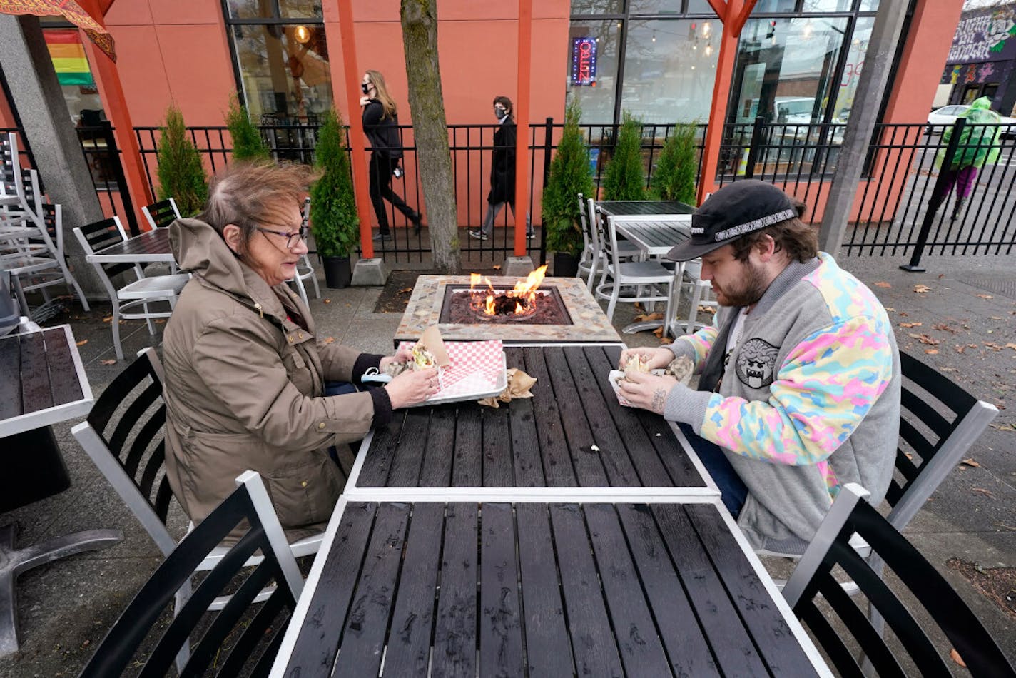 Diners Bonnie Breitman, left, and Casey McGan huddle near an outdoor gas fire as they eat lunch outside in a blustery wind Tuesday, Nov. 17, 2020, in Bellingham, Wash. Washington Gov. Jay Inslee on Sunday announced tighter restrictions in the state in response to a flood of new cases of COVID-19. Indoor social gatherings will be prohibited unless attendees have quarantined for 14 days or tested negative for COVID-19 and quarantined for a week.