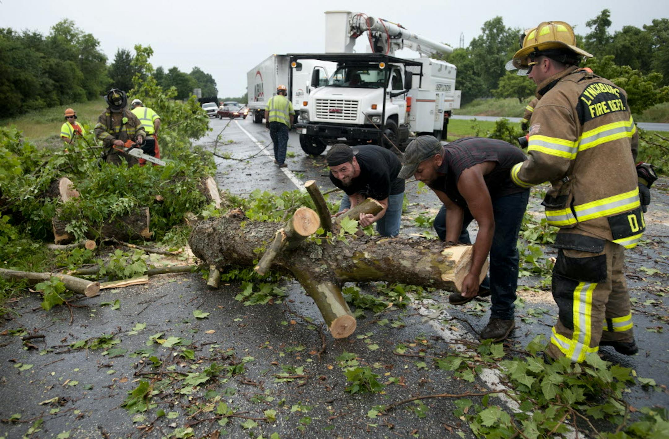 Passing motorists Charles Jenkins (center) and Tyler Hackworth (center right) work with members of the Lynchburg Fire Department to clear a tree that fell due to heavy winds across the southbound lanes of U.S. 501 in Lynchburg, Va., Thursday.