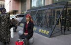 FILE - In this May 1, 2014 file photo, a Uighur woman rests near a cage protecting heavily armed Chinese paramilitary policemen on duty in Urumqi in C