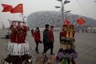 In this picture taken, Sunday, Feb. 23, 2014, tourists pass by memorabilia on sale near the iconic Bird's Nest National Stadium in Beijing, China. The
