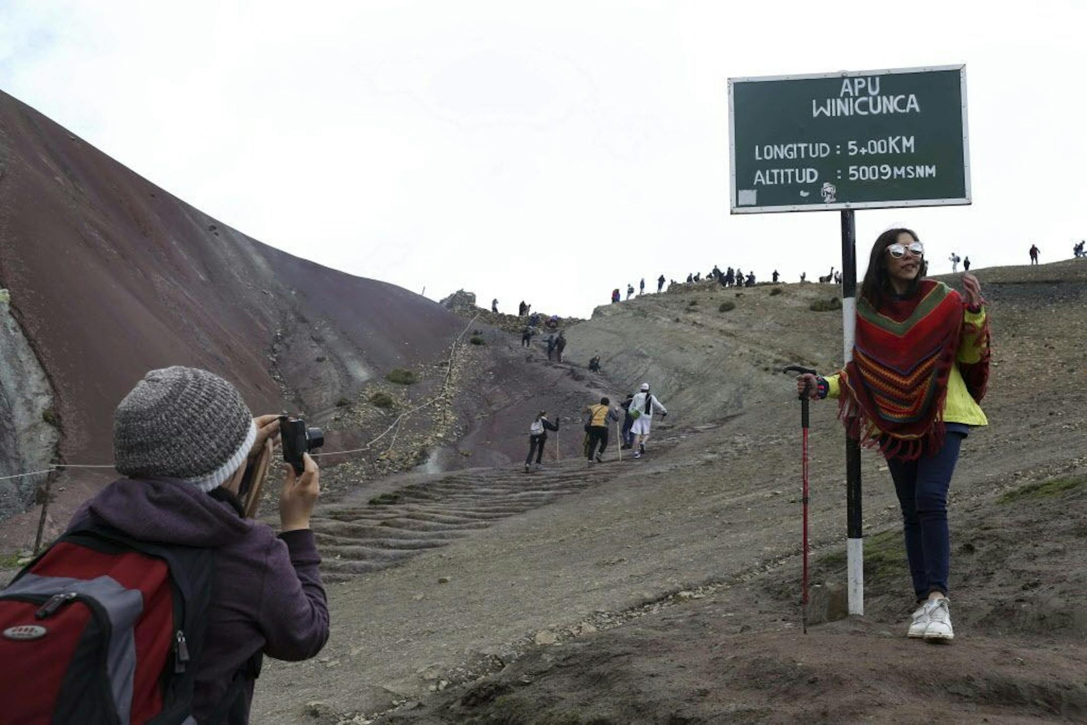 In this March 2, 2018 photo, a tourist poses for a photo at the entrance that leads to Rainbow Mountain, in Pitumarca, Peru. Backpackers are flocking to the dazzling rainbow-colored mountain in the Peruvian Andes, transforming a forgotten village of impoverished alpaca herders into a tourist mecca.