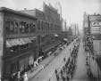 A parade on 4th Street passing by the Grand Arcade in 1907. The towered building to the rear is the old St. Paul City Hall-Ramsey County Courthouse, r