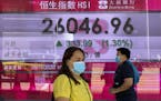 People walk past a bank's electronic board showing the Hong Kong share index at Hong Kong Stock Exchange Monday, Nov. 9, 2020.