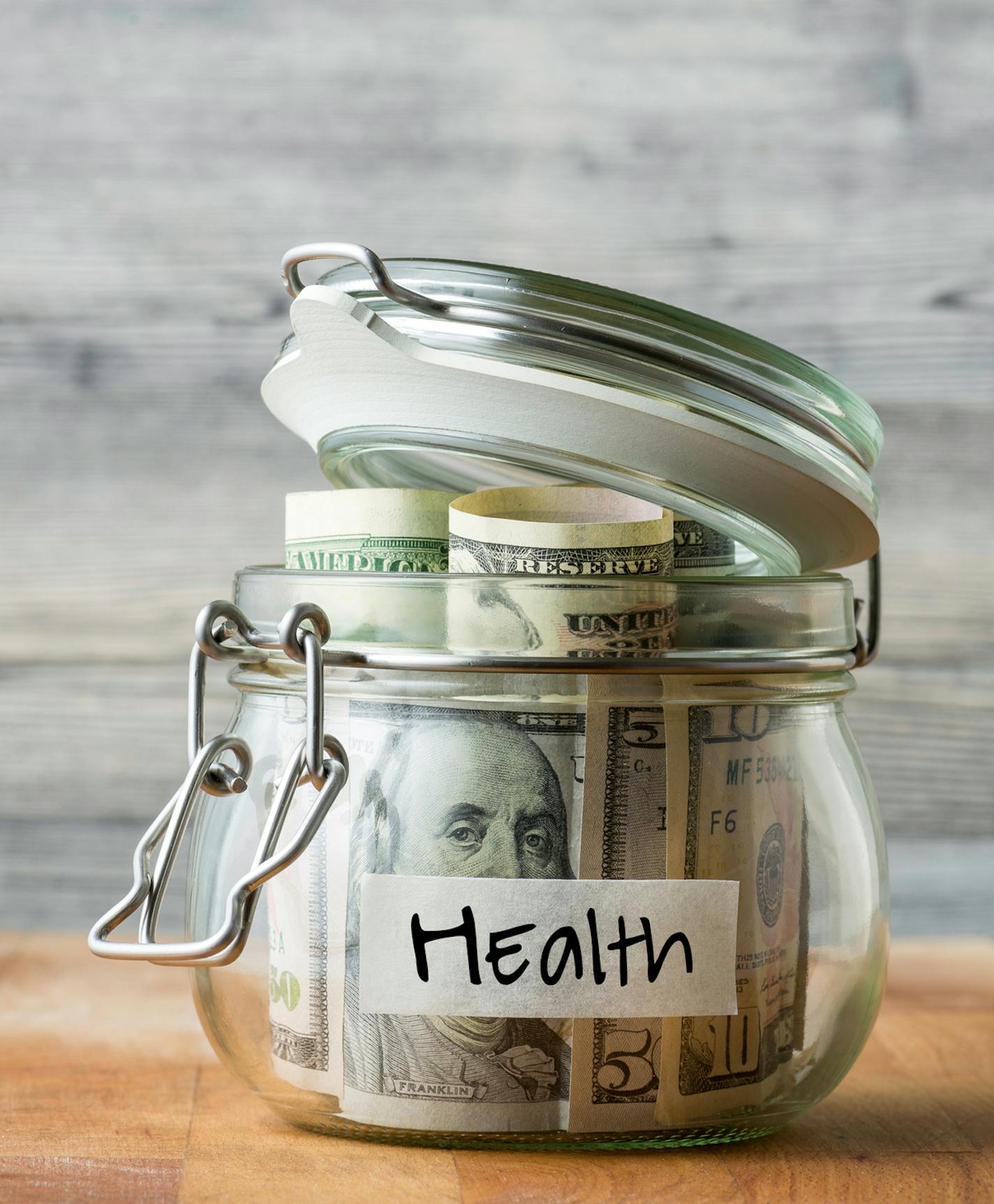 Dollar bills in glass jar isolated on wooden background. Saving money for health.