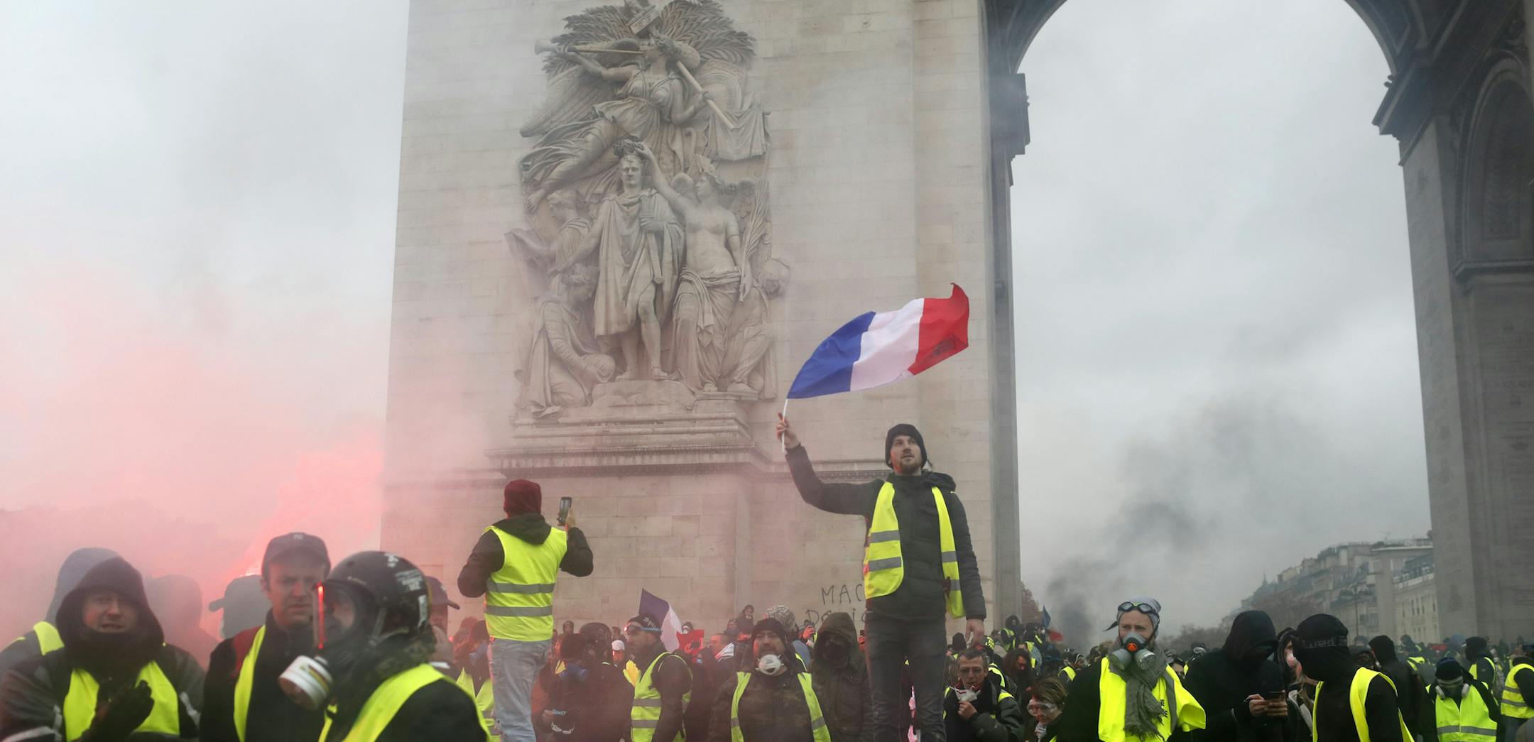A demonstrator wearing a yellow jacket waves a French flag at the Arc de Triomphe during a demonstration Saturday, Dec.1, 2018 in Paris. Protesters angry about rising taxes clashed with French police for a third straight weekend and over 100 were arrested after pockets of demonstrators built barricades in the middle of streets in central Paris, lit fires and threw rocks at officers Saturday. (AP Photo/Thibault Camus)