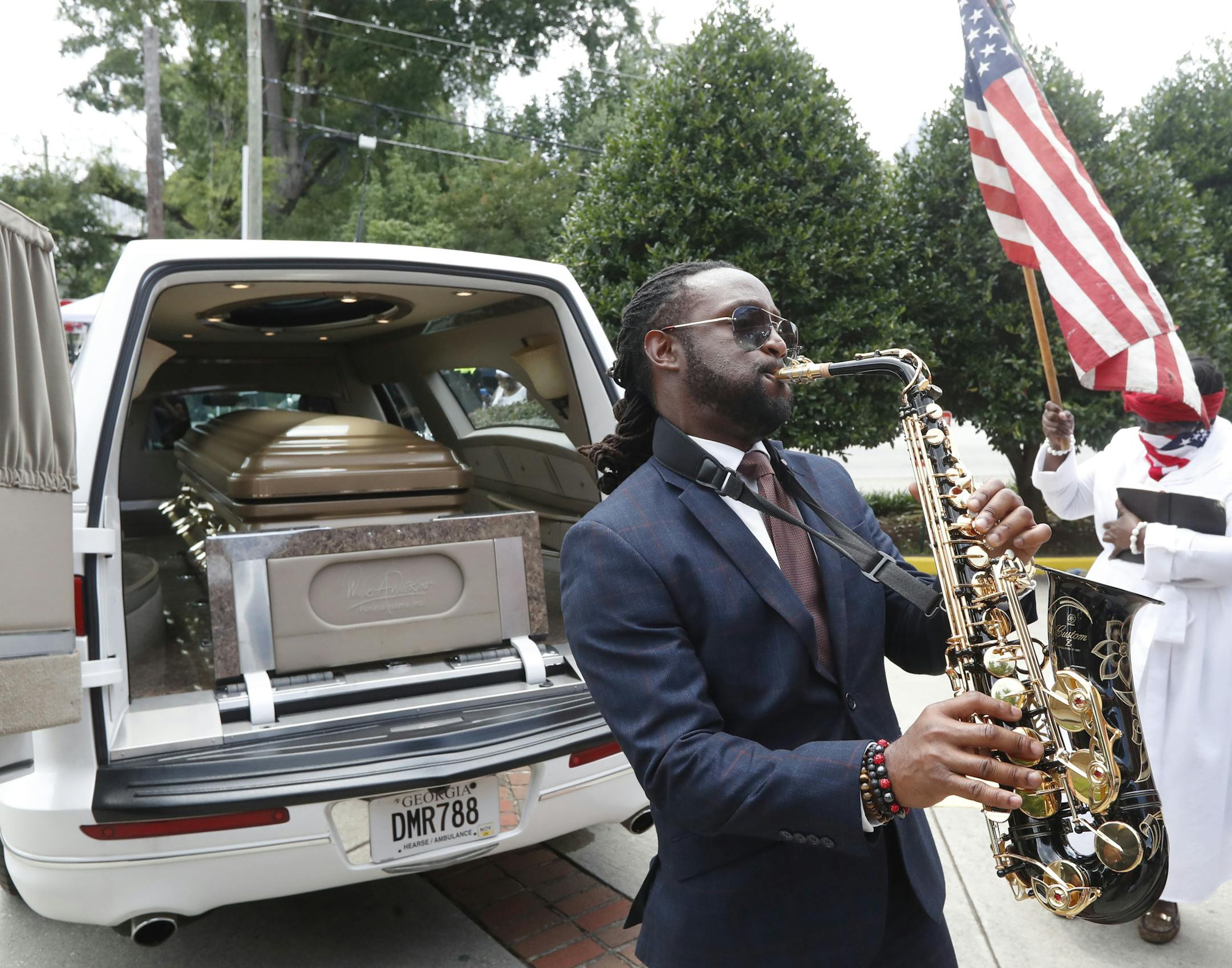 A musician plays music near the hearse carying the casket of Rayshard Brooks, Tuesday, June 23, 2020, in Atlanta. The funeral for Brooks was held today. Brooks died after being fatally shot by an Atlanta police officer. (AP Photo/John Bazemore)