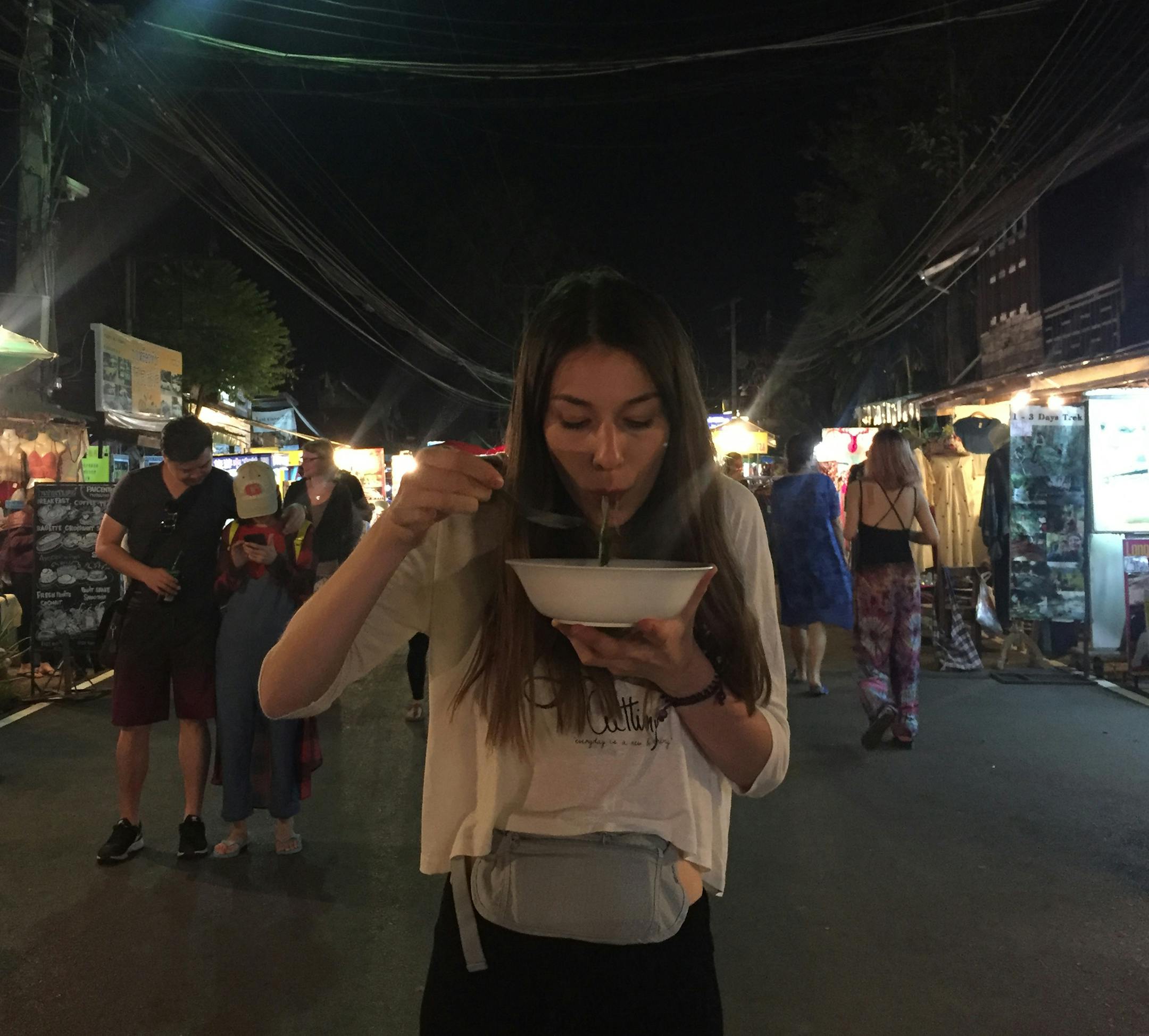 Cat Di Stasio eating a bowl of noodles in a street market in Pai, Thailand. Traveling together forces friendships to skip a few steps, causing you to get closer faster.