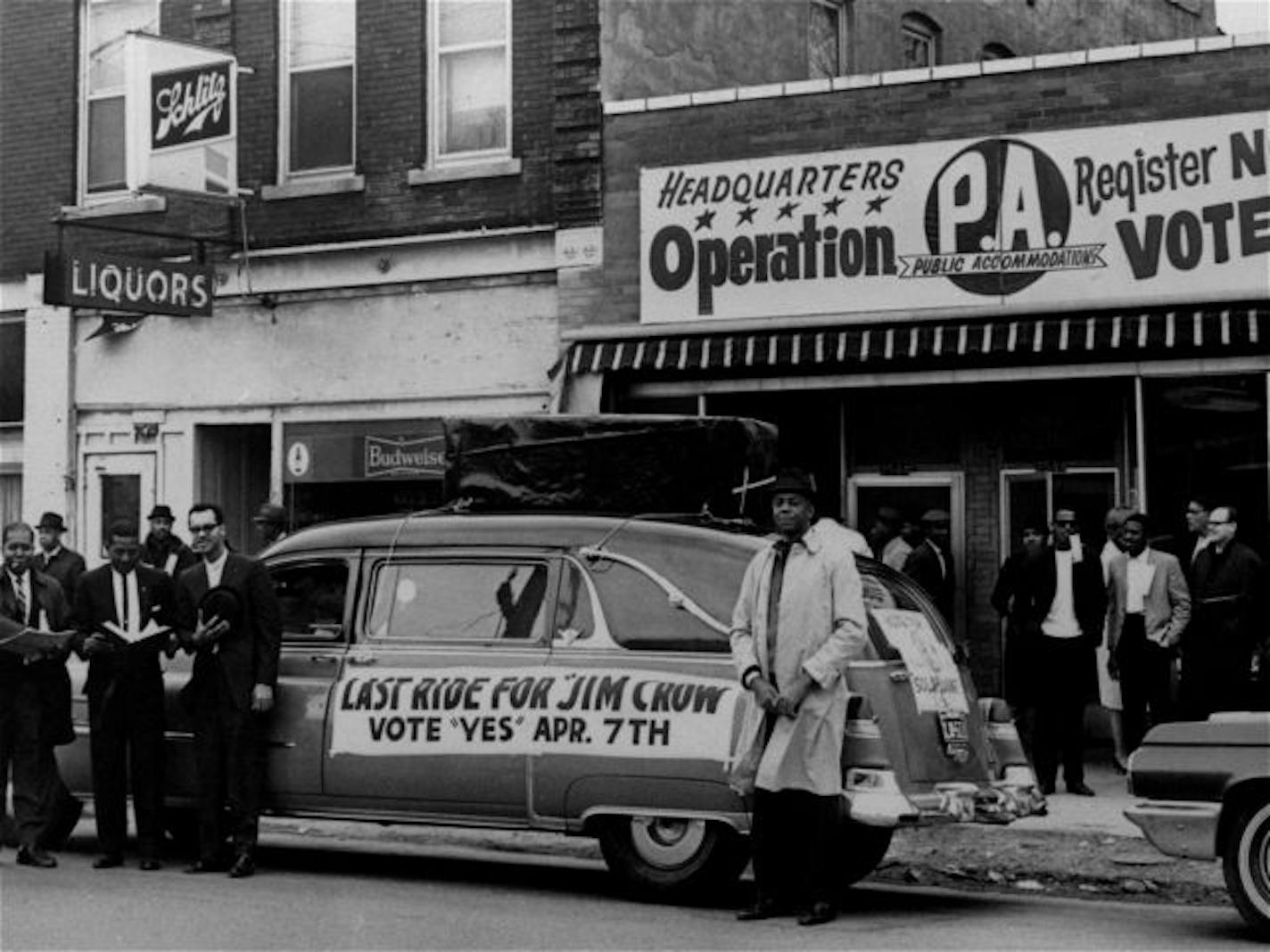 A hearse with a casket mounted on its top and a sign reading: Last Ride For Jim Crow, is parked in front of headquarters for workers favoring approval of Kansas City's Public Accommodations ordinance that was being voted on in a referendum election April 7, 1964.