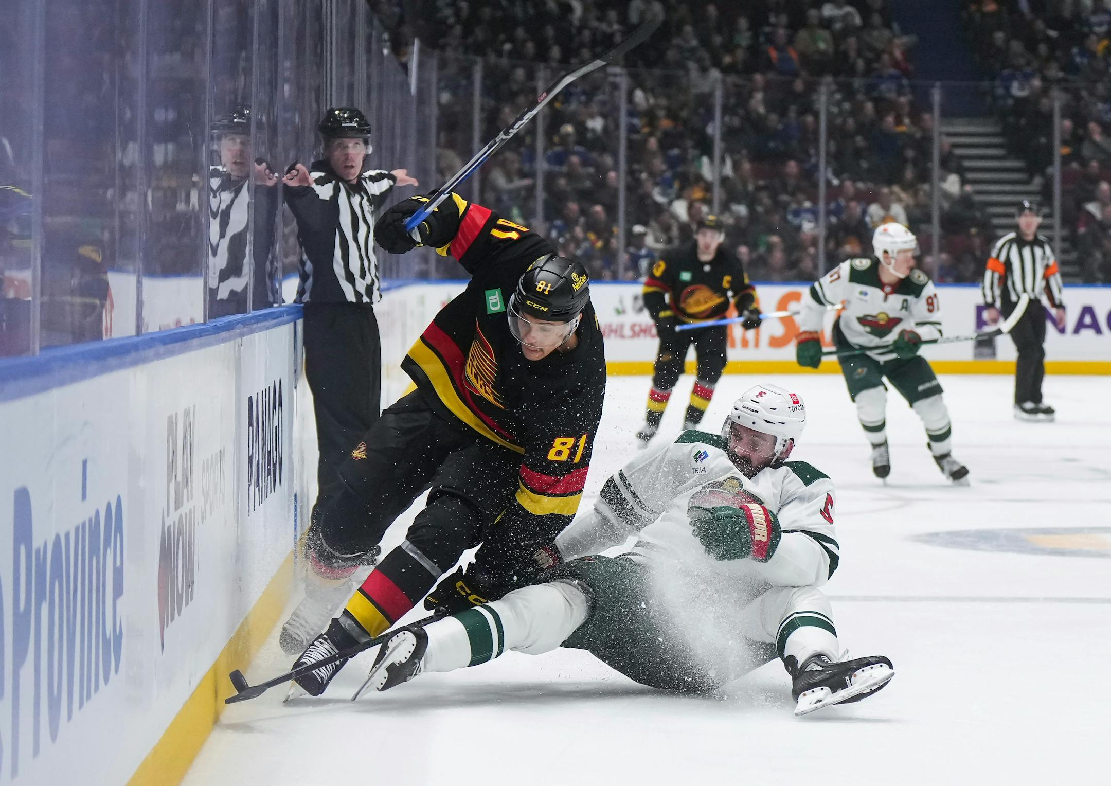 Minnesota Wild's Jacob Middleton, right, falls while vying for the puck against Vancouver Canucks' Dakota Joshua during the second period of an NHL hockey game Thursday, Dec. 7, 2023, in Vancouver, British Columbia. (Darryl Dyck/The Canadian Press via AP)