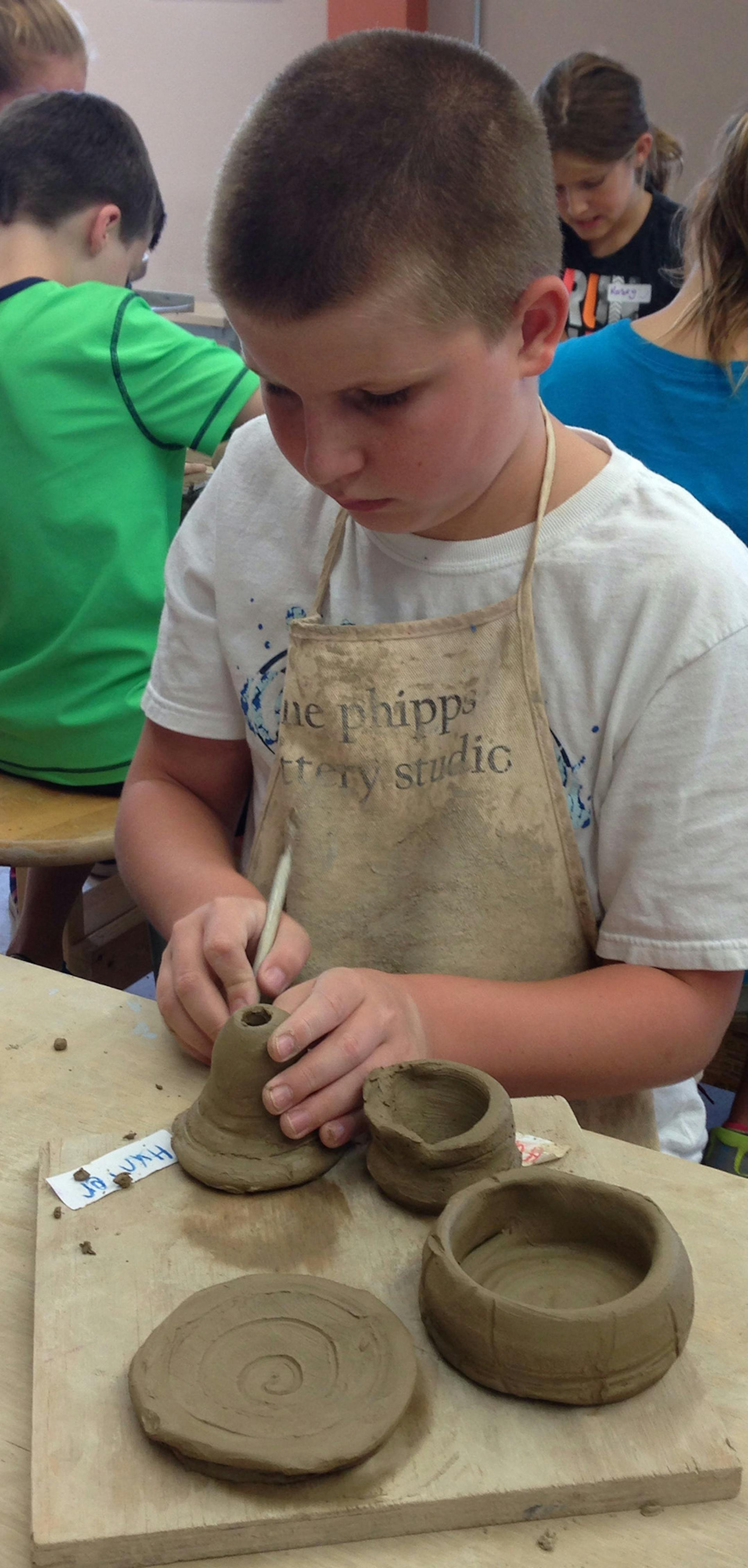 Hunter Eno (Hudson) trimming bowls, a vase, and a small plate he made during a Pottery on the Wheel summer class in The Phipps Ceramic Studio.