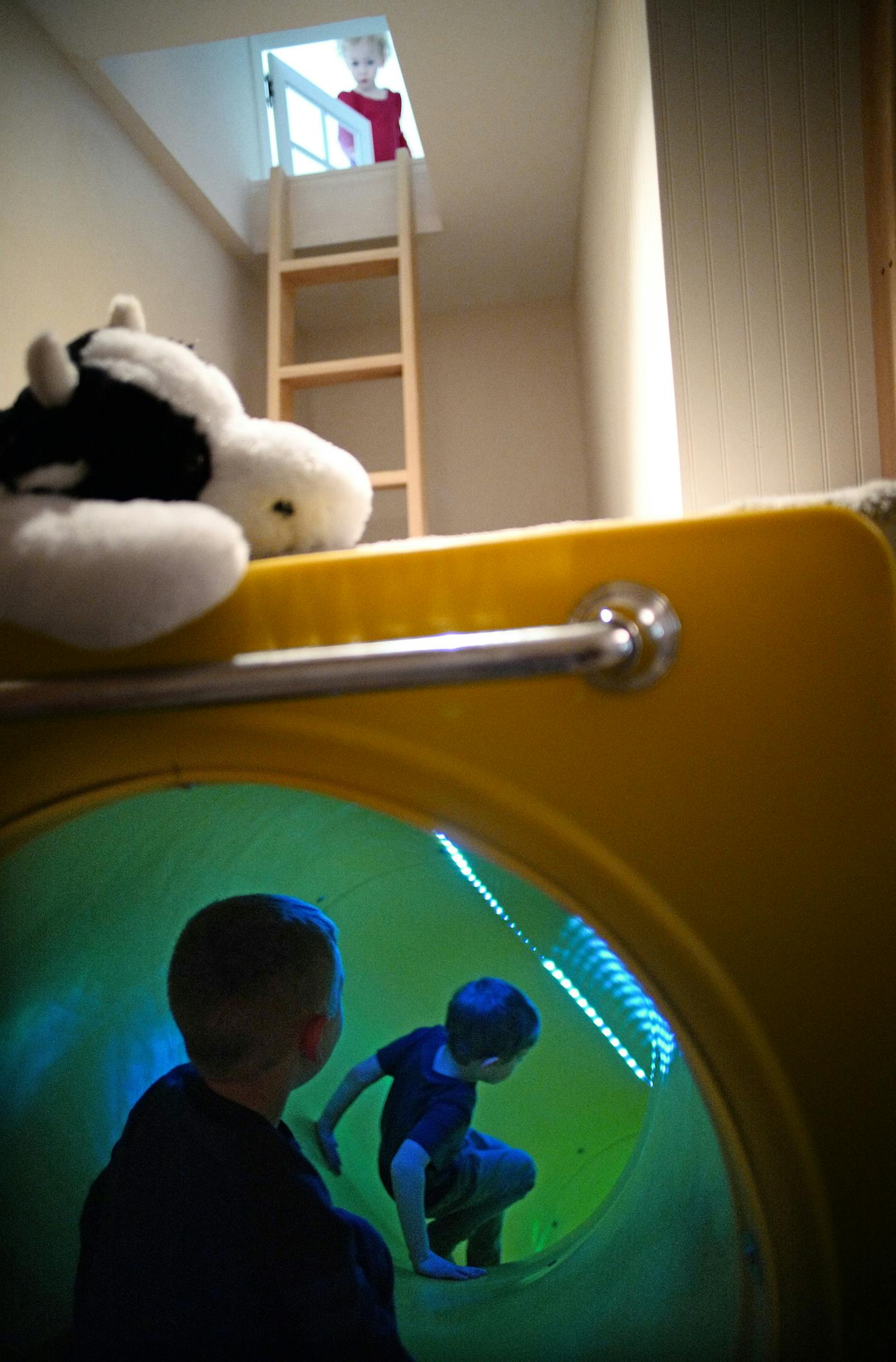 Neighbor Elliot Budziak, 3, plays with Leo Kuhl, 6, in the slide while sister Charlie, 3, looks through a door that leads down a ladder on the second floor.