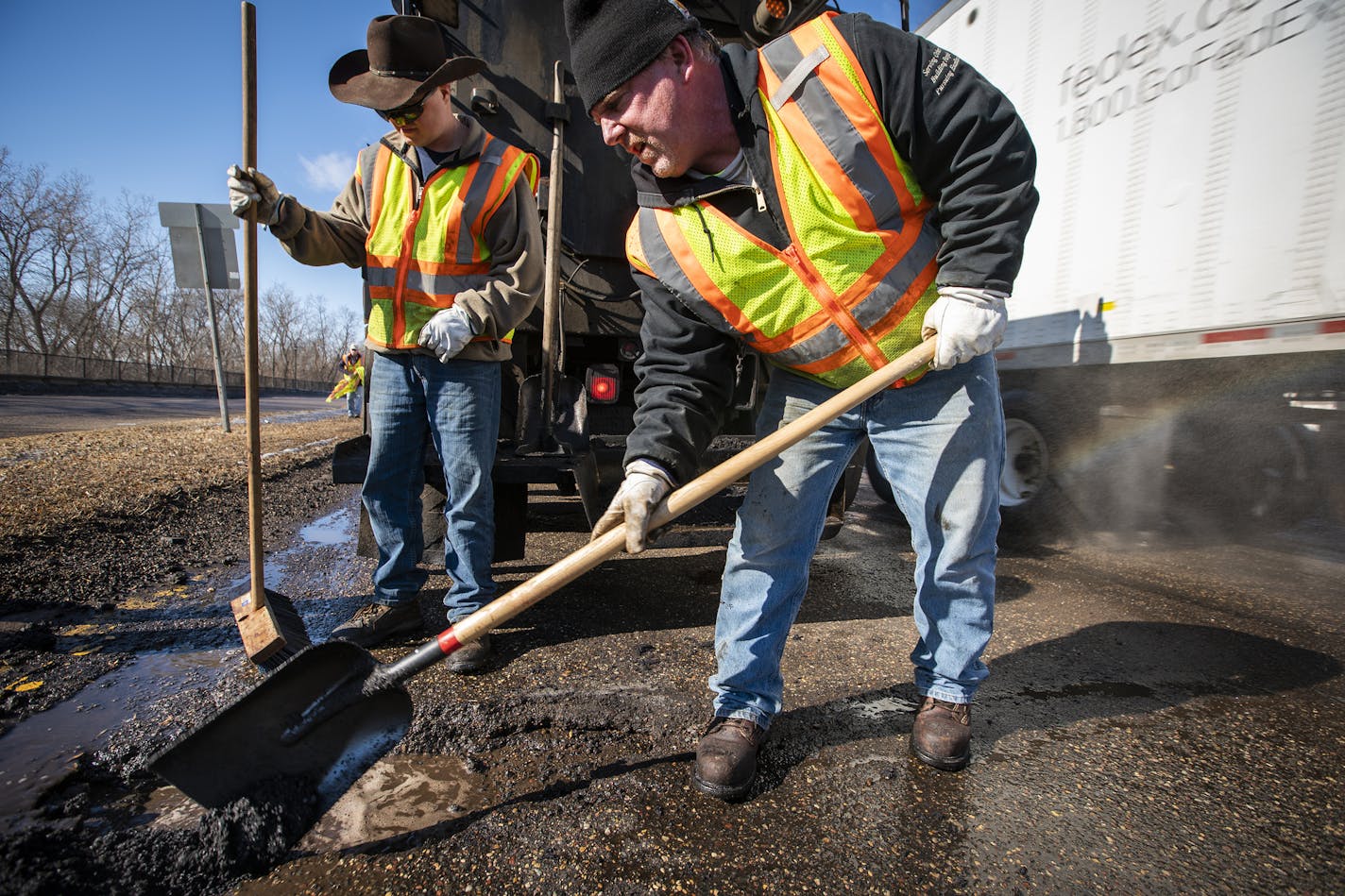 Street service workers Bradley Therres, from left, and Lance Hamby fill potholes with asphalt on Shepard Road as a truck goes by on the right side of the road.