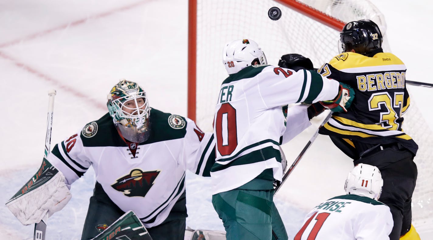 Minnesota Wild goalie Devan Dubnyk, left, eyes the puck as Minnesota Wild defenseman Ryan Suter tries to clear away Boston Bruins center Patrice Bergeron.