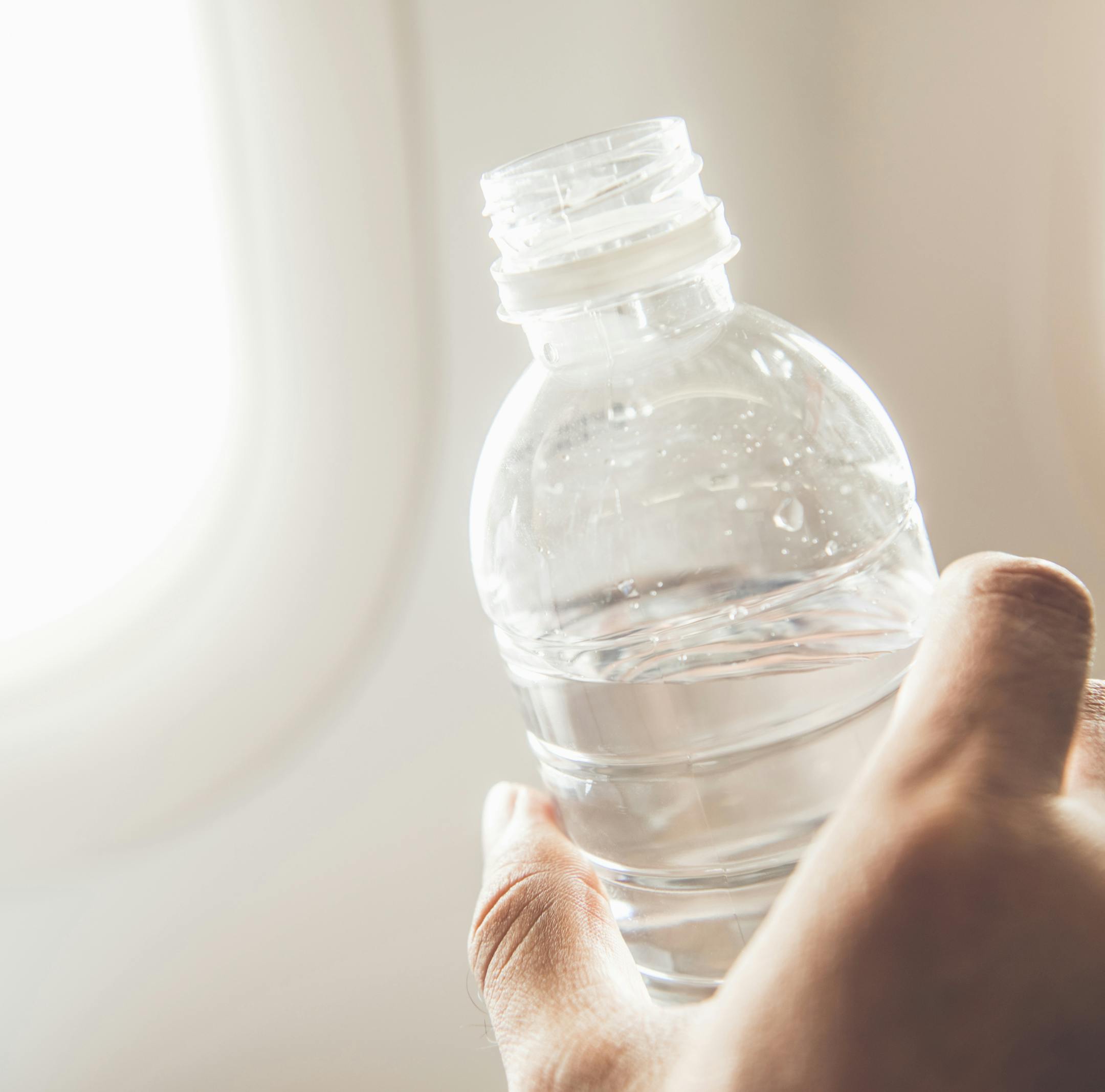 Passenger holding bottle of water about to drink preventing dehydration while traveling on the plane