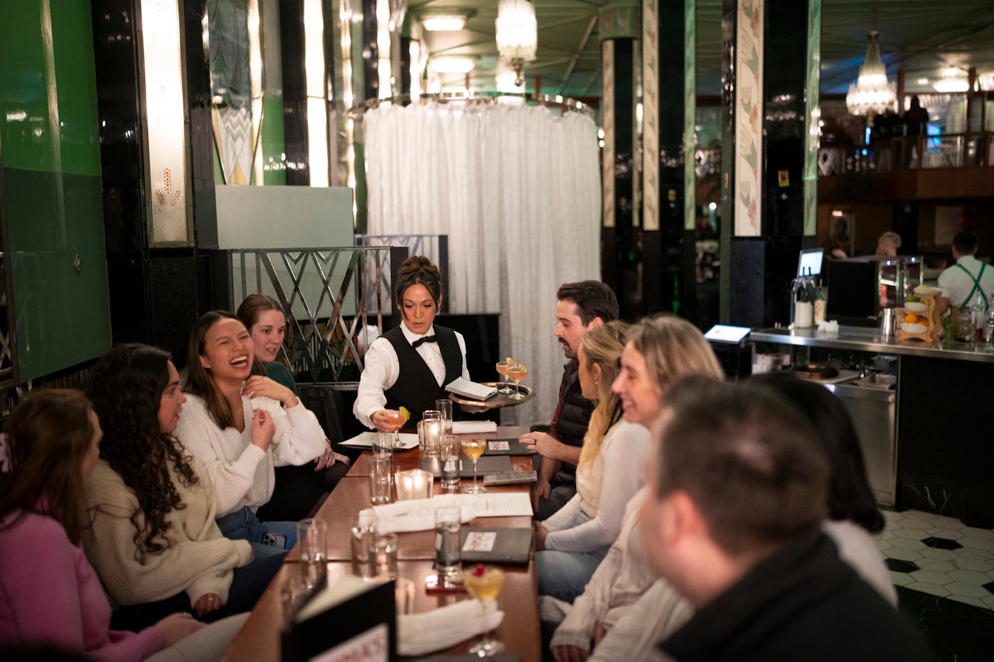 Server Amy Walrath serves a group of friends who work in the Minneapolis City Center building and had gathered after work for drinks and dinner to celebrate a going away party for their colleague Maddy Chow (in white sweater laughing) at Fhima's on Wednesday, Dec. 13, 2023 in Minneapolis, Minn. The friends occationally like to go to Fhima's for happy hour. ] RENEE JONES SCHNEIDER • renee.jones@startribune.com