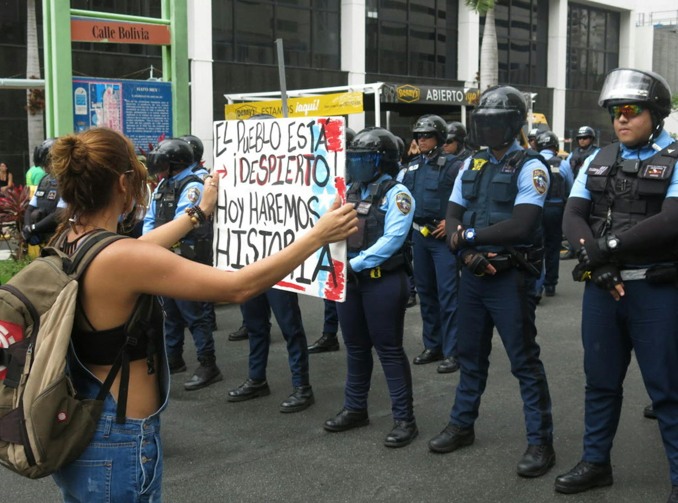 A woman holds a sign up to police that reads in Spanish "The people are awake. Today we'll make history" during a May Day protest against looming austerity measures amid an economic crisis and demanding an audit on the island's debt to identify those responsible in San Juan, Puerto Rico, Monday, May 1, 2017. Puerto Rico is preparing to cut public employee benefits, increase tax revenue, hike water rates and privatize government operations, among other things. (AP Photo/Danica Coto)