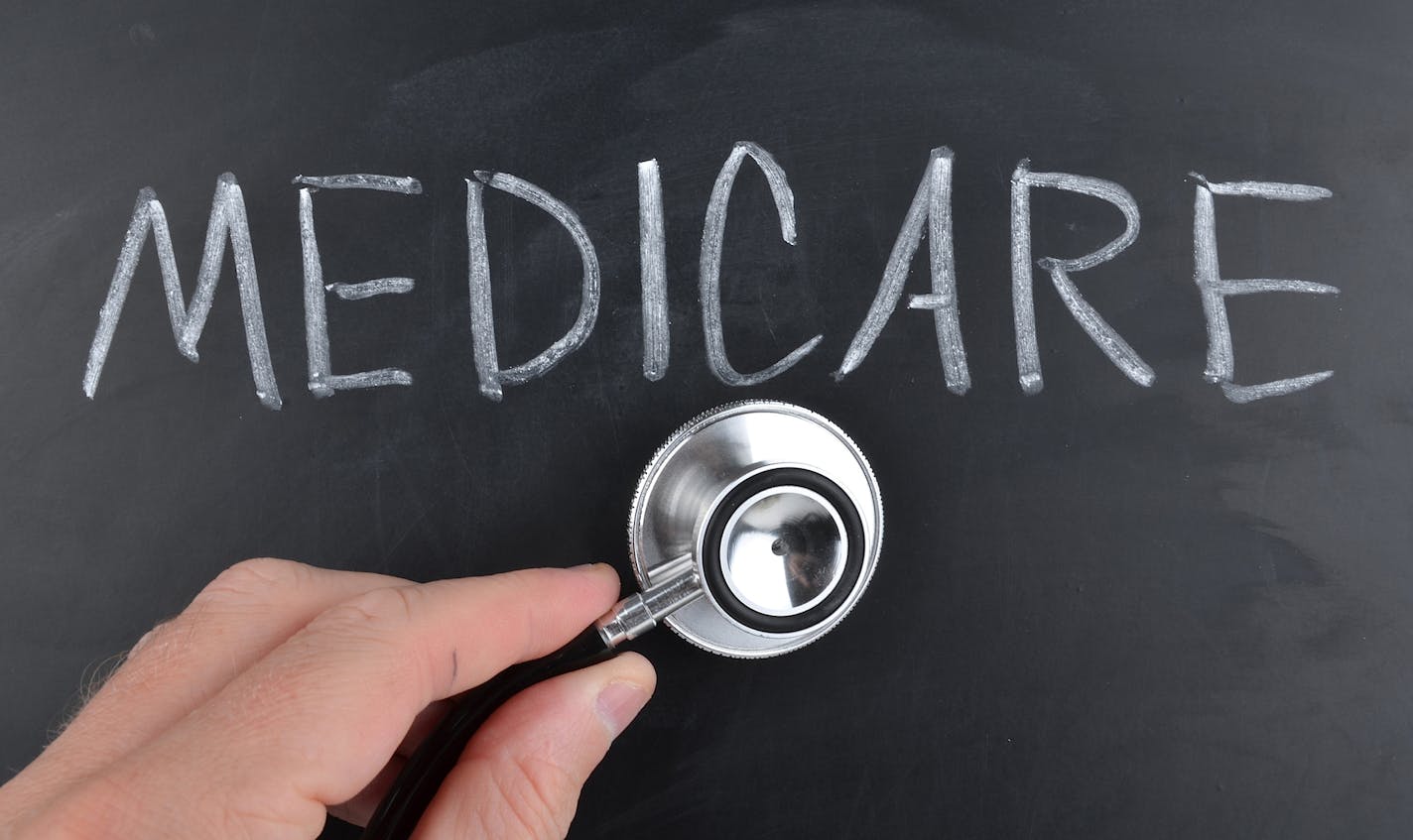 iStock
Medicare written on a blackboard in white chalk with a doctor using a stethoscope to check up.