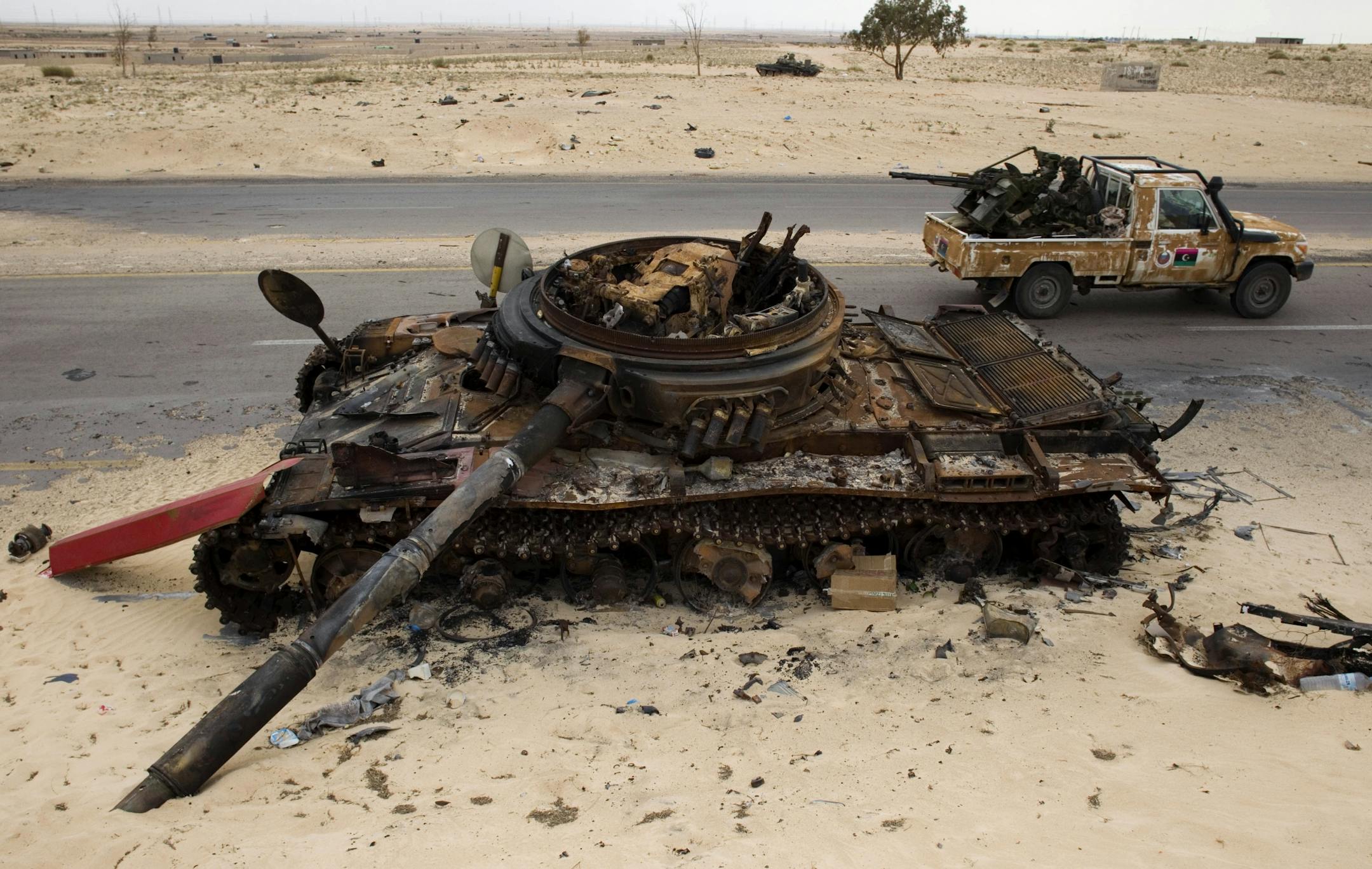 Libyan rebel fighters drive by a previously destroyed pro-Gadhafi forces tank as they make their way to the frontline, on the outskirts of Ajdabiya, Libya, Wednesday, April 20, 2011. Moammar Gadhafi's loyalists shelled the Nafusa mountain area and clashed with opposition forces in the besieged coastal city of Misrata Wednesday, rebels said, as the Libyan leader also sought to quell resistance in the western part of the country that is largely under his control.