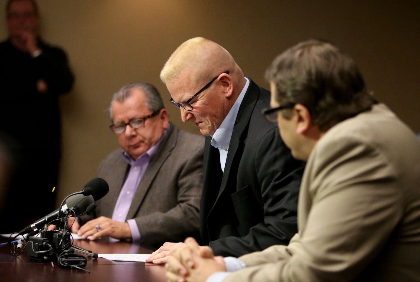 St. Paul Central High teacher John Eklbad, center, appears to grimace in pain while switching chairs before speaking to media members Tuesday, Dec. 22, 2015, at his attorneys' Bloomington MN, office. Ekblad recounted injuries and what he remembers of an assault by a student at St. Paul Central High on Dec. 6 that has left him with a head injury and constant headaches. He is flanked by his attorneys Philip Villaume, left, and Jeffrey Schiek, right.](DAVID JOLES/STARTRIBUNE)djoles@startribune.com