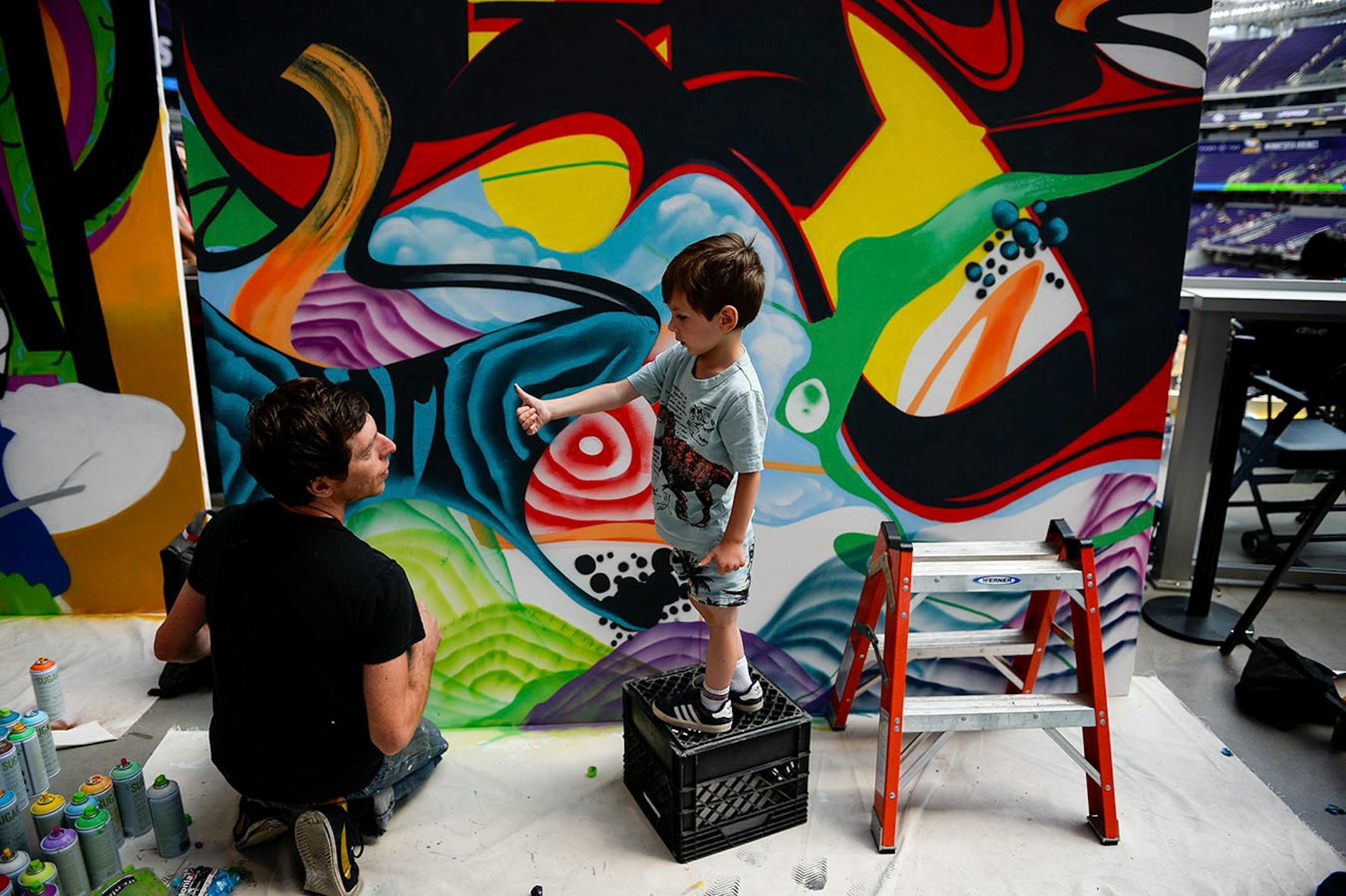 Sonny Broder, 4, showed his father, Andrew, some paint he got on his thumb as Andrew worked on spray painting a mural inside US Bank Stadium Sunday.