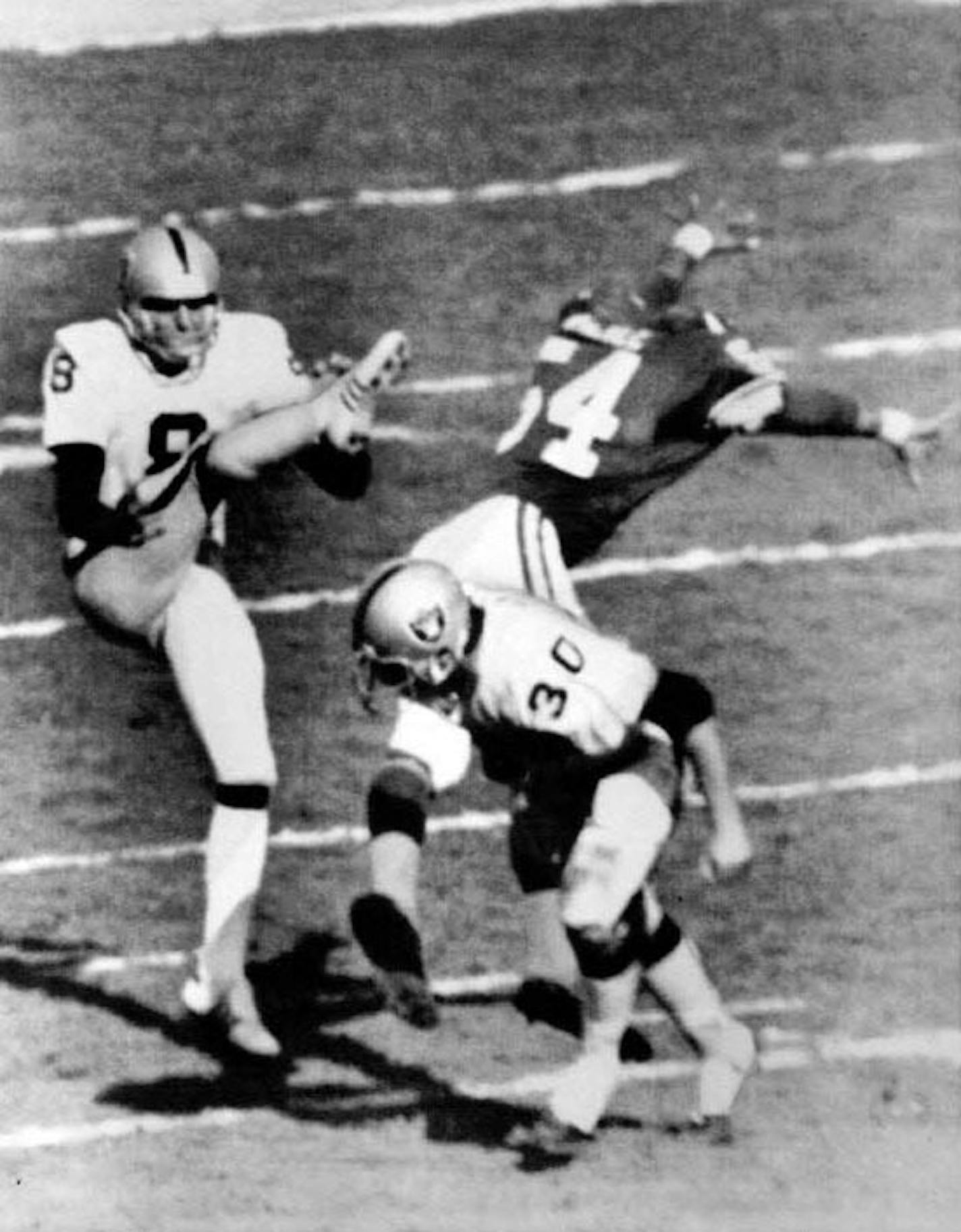 In Super Bowl XI, Minnesota's Fred McNeill (54) blocked the first punt ever in four years of NFL punting for Oakland's Ray Guy as the Raiders' Mark Van Eeghen (30) missed a block.