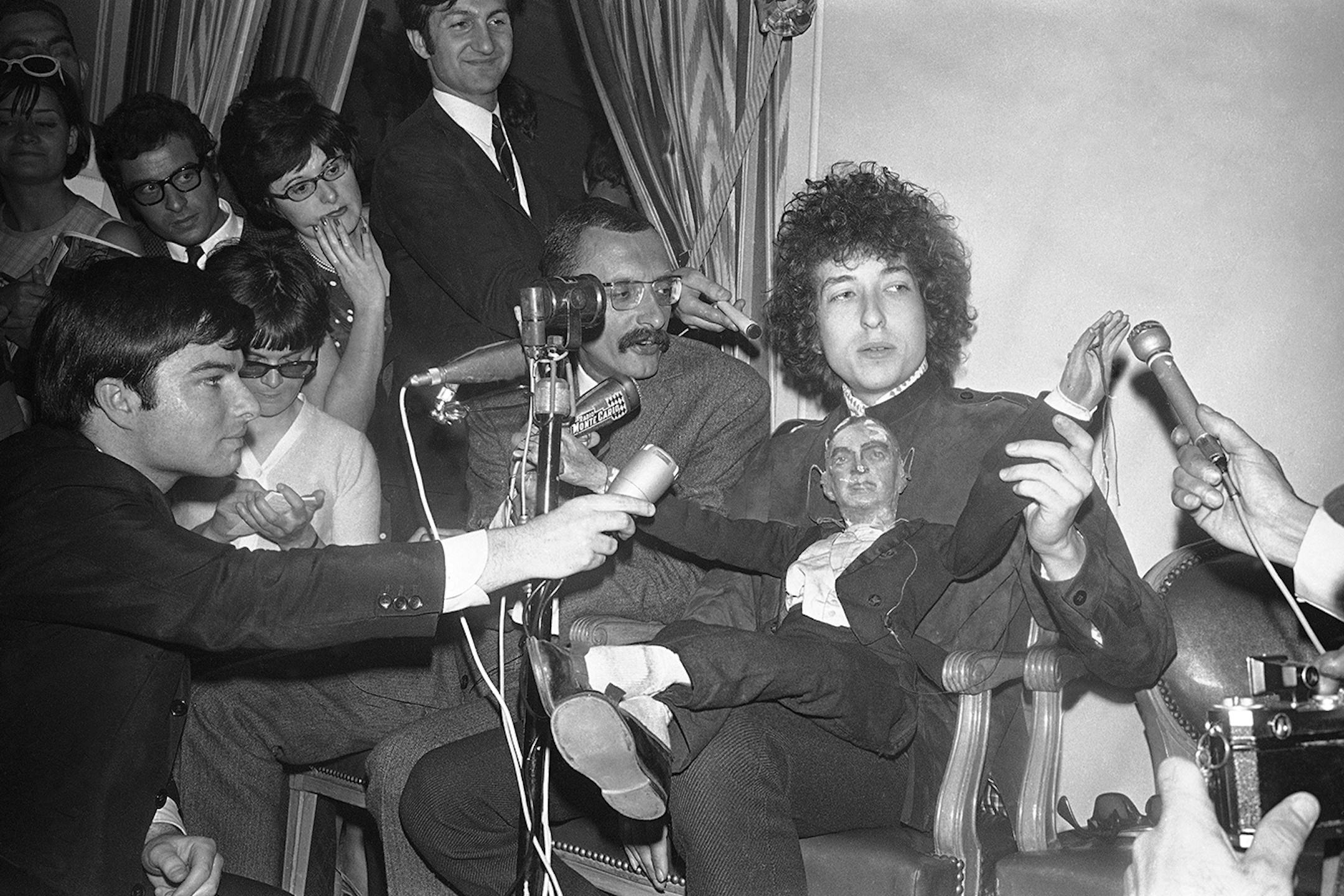 American folk singer Bob Dylan sits with a puppet as he faces the media during a press conference at the Hotel George V in Paris, France on May 23, 1966. He will appear on Tuesday at the Paris Olympia music-hall.