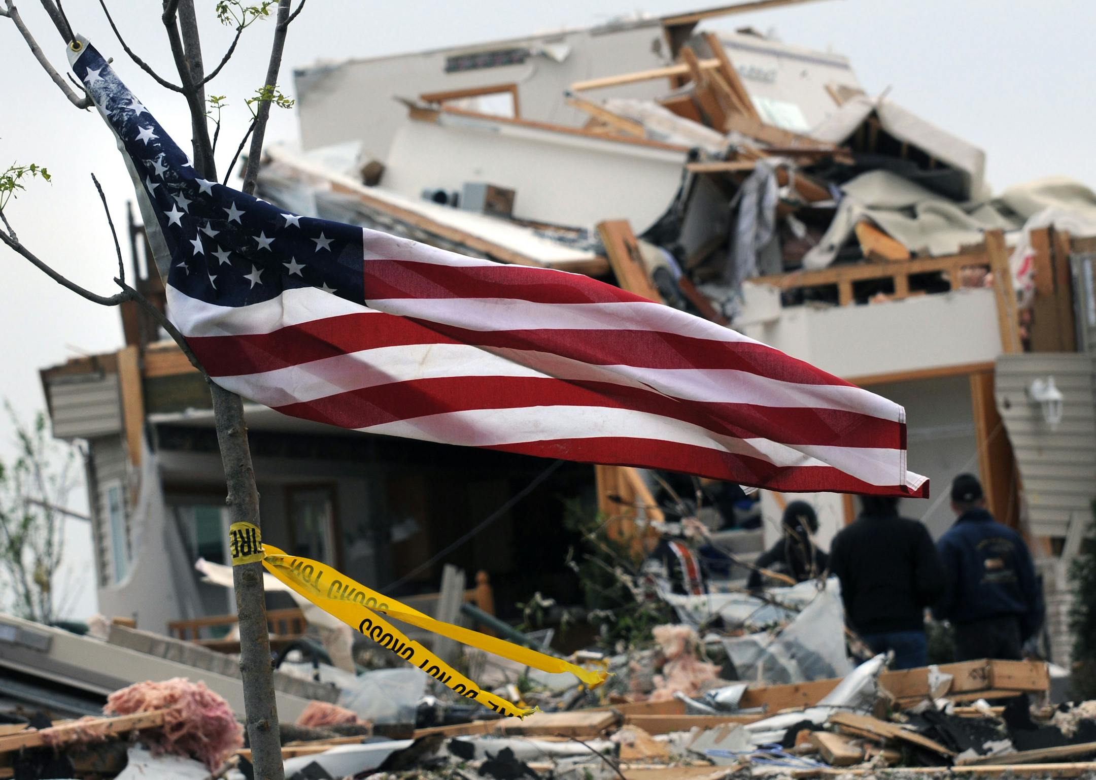 An American flag and police tape flapped in the breeze Tuesday outside a house destroyed by Sunday's tornado. Many in Hugo spent the day going through the remains of their homes.