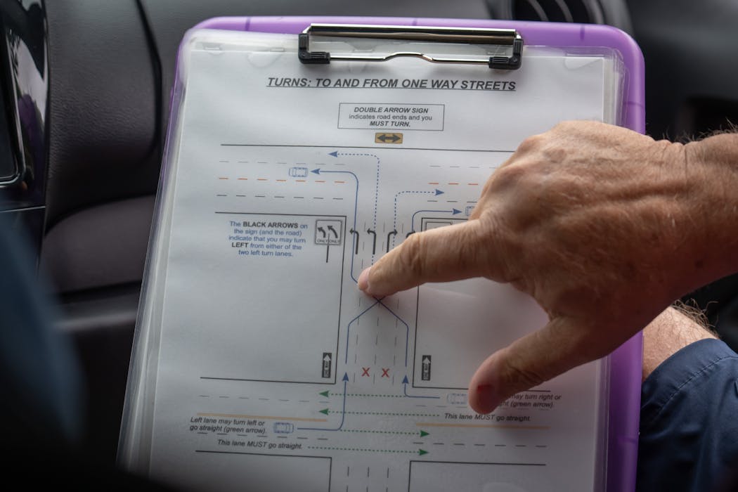 Dale Robinson, who owns Ken's Driving School, points at printed driving instructions while teaching a behind the wheel lesson in Columbia Heights.