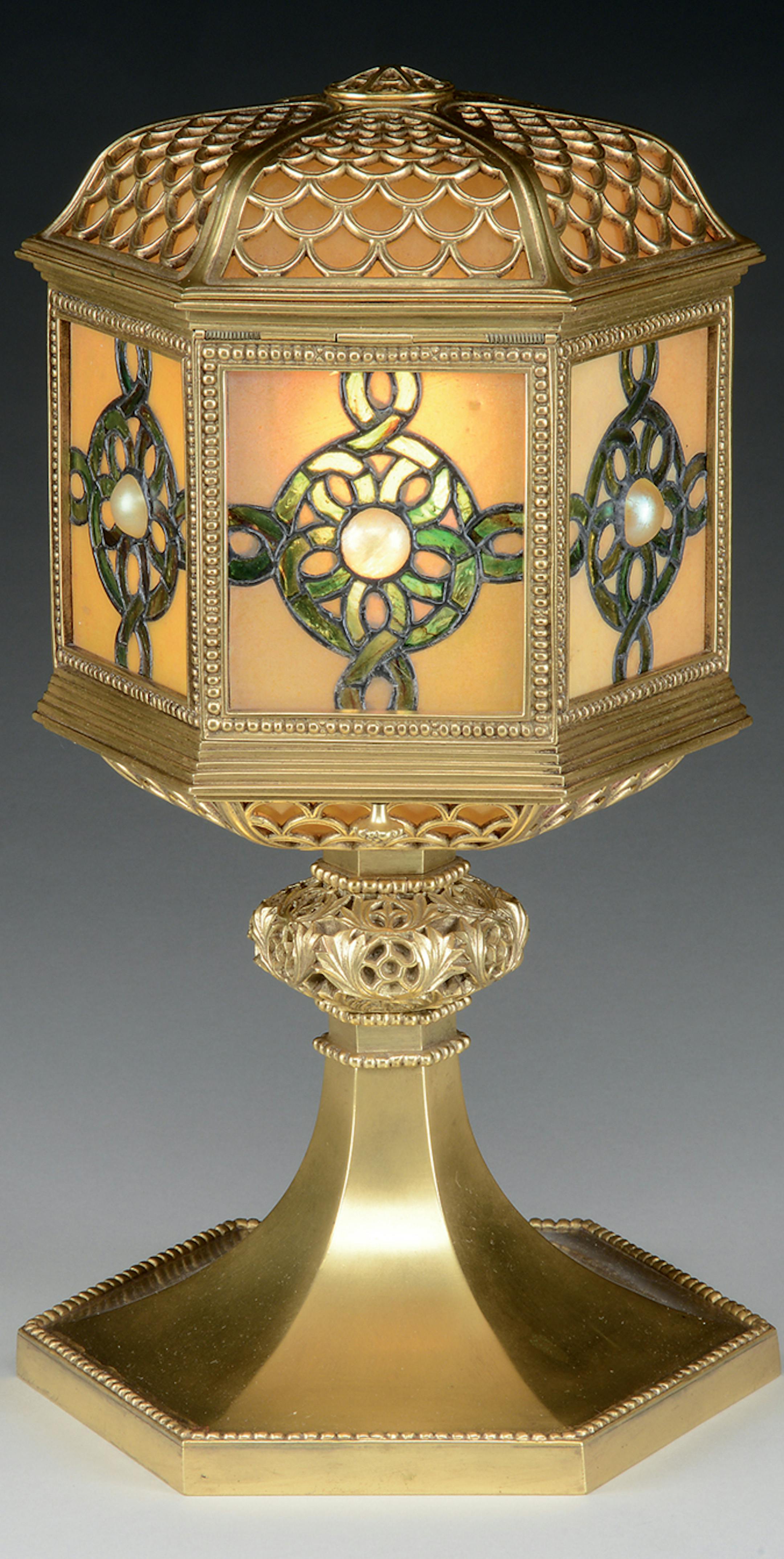 This 15 [1/2]-inch-tall table lantern marked "Tiffany Studios New York" sold for $6,655 at a recent James D. Julia auction in Maine. It has a shade with glass panels centered with a cabochon jewel. The stem is decorated bronze with a gold patina.
credit: James D. Julia Inc.