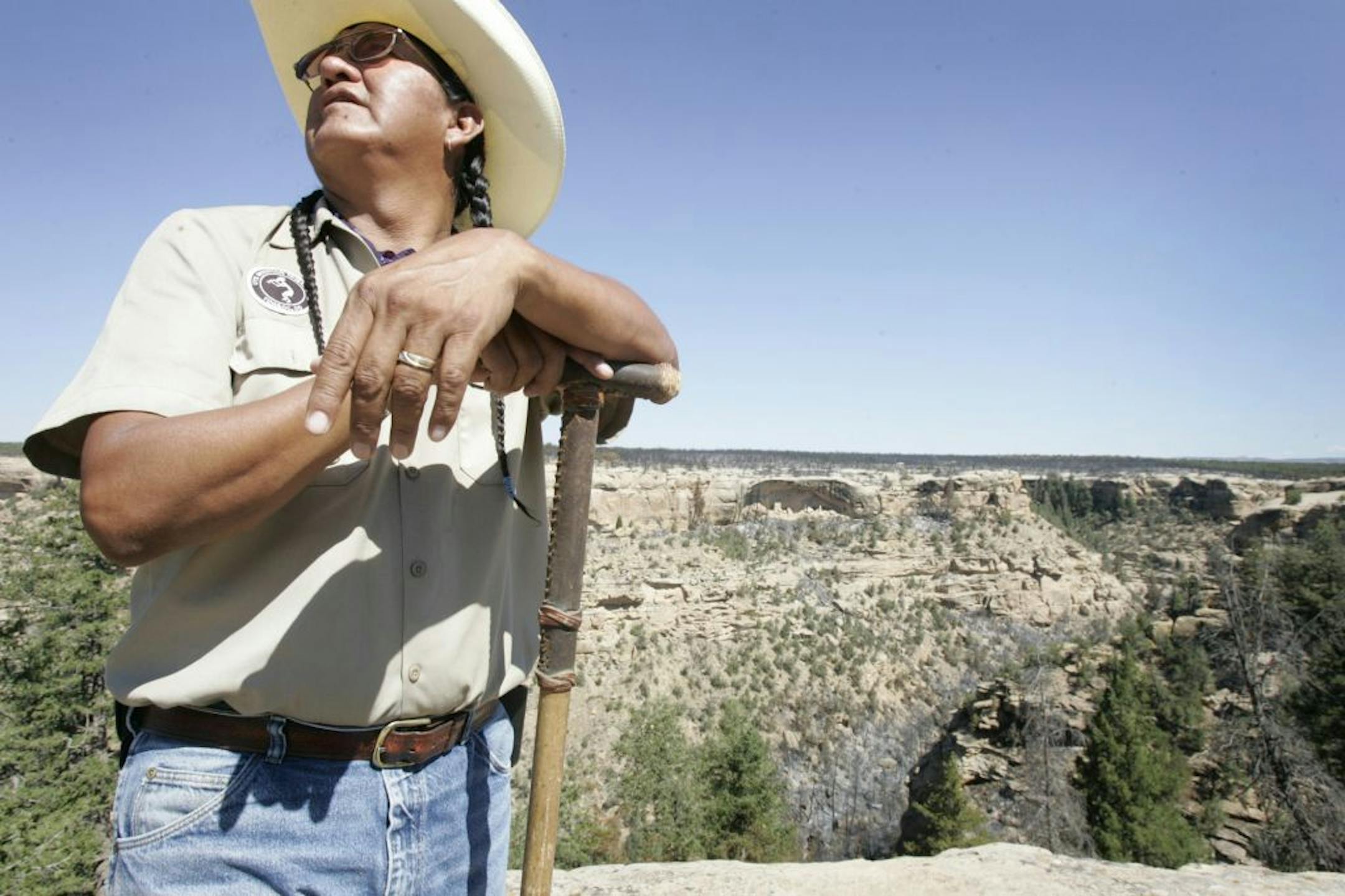 Rickey Hayes, senior tour guide in the Ute Mountain Tribal Park stand with the Lion House cliff dwelling in the background.