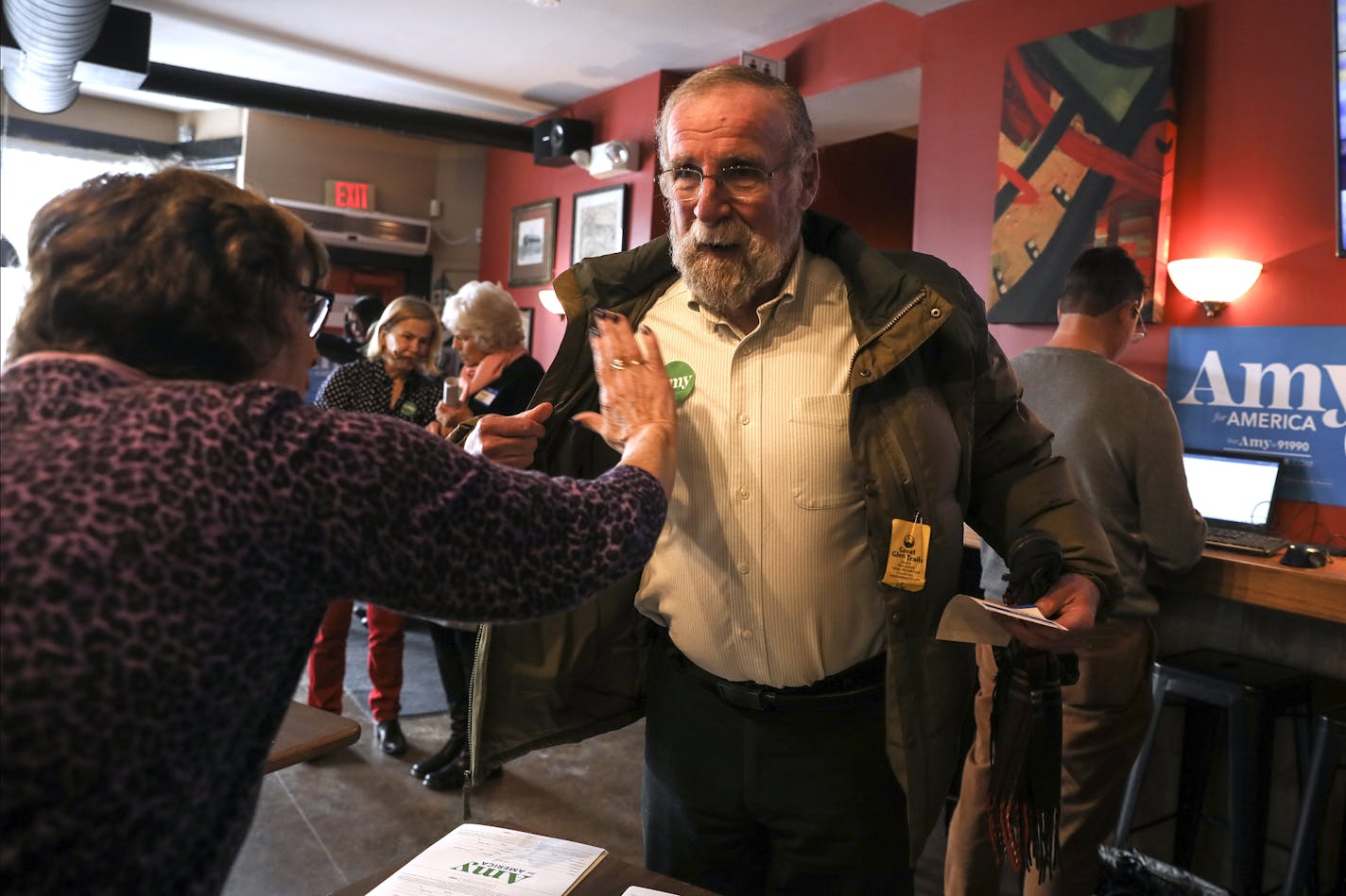 A volunteer puts an Amy For America sticker on Bob Jones shirt as he arrives to hear Sen. Amy Klobuchar, D-Minn., speak at The Village Trestle in Goffstown, N.H. Monday, Feb. 18, 2019: (AP Photo/ Cheryl Senter)