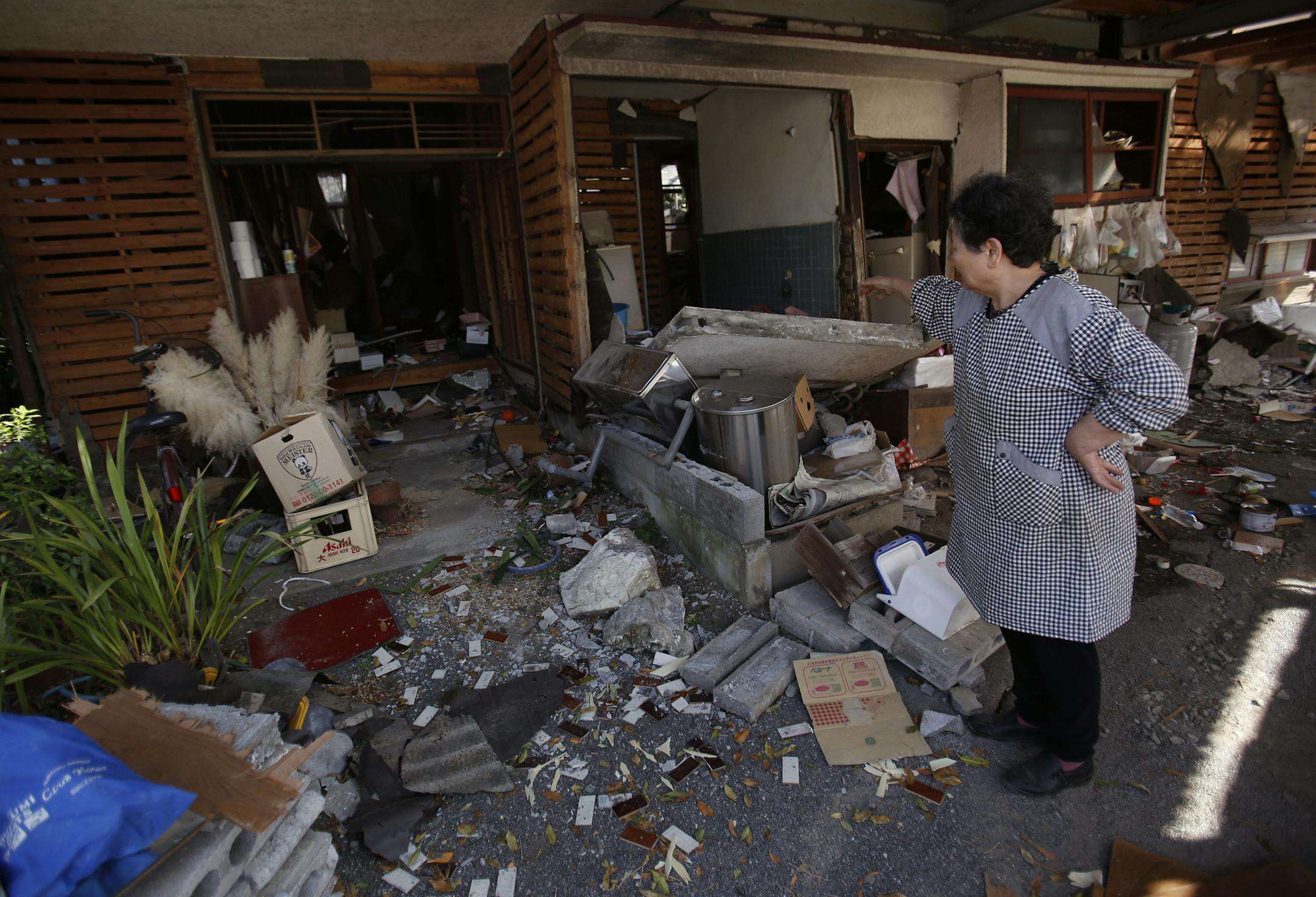 A local resident cleans up her house in Mashiki, Kumamoto prefecture, southern Japan, Friday, April 15, 2016. Aftershocks rattled communities in southern Japan as businesses and residents got a fuller look Friday at the widespread damage from an unusually strong overnight earthquake. (AP Photo/Koji Ueda)