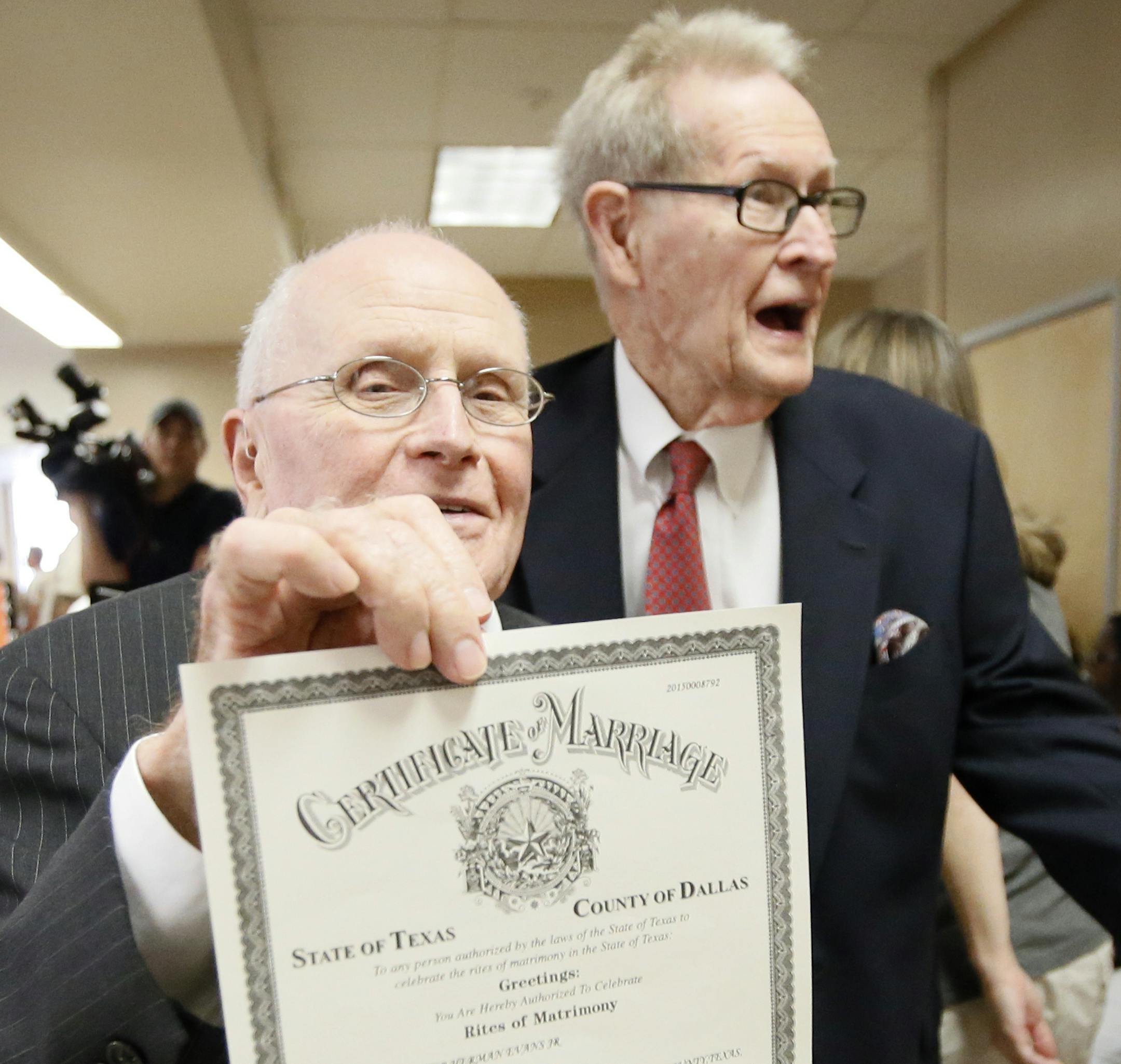 George Harris, left, 82, walks out of the Dallas County Clerks office showing his marriage license as his husband Jack Evans, holding roses, 85, follows behind Friday, June 26, 2015, in Dallas. Harris and Evans were the first same sex couple to be married in Dallas after receiving their license. Gay and lesbian Americans have the same right to marry as any other couples, the Supreme Court declared Friday in a historic ruling deciding one of the nation's most contentious and emotional legal quest