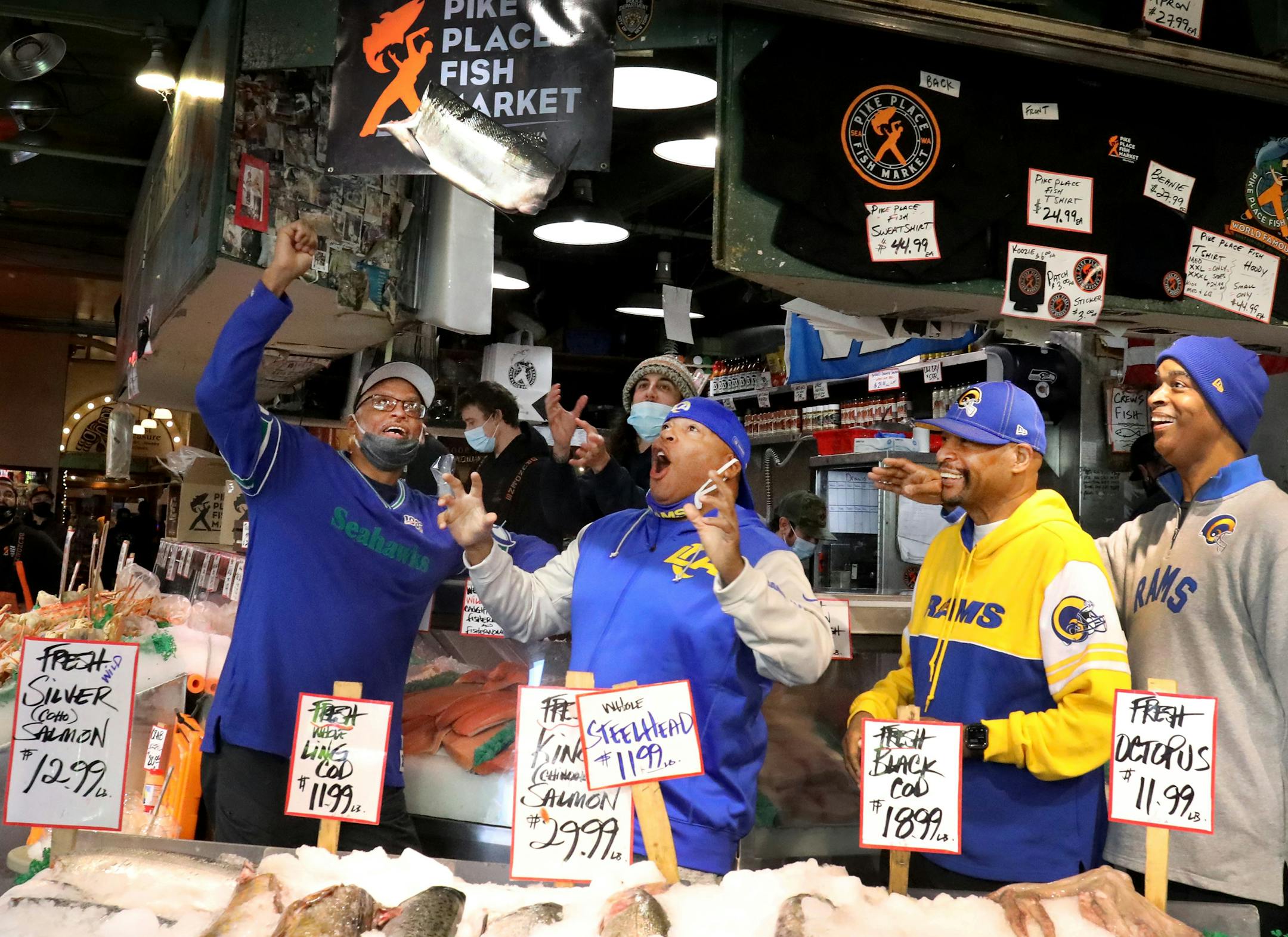 Visiting football fans Hugh Roberts, left, Eric Paris, his brother Kevin Paris and Tony Laughton get a kick out of the "flying fish" at the famous Pike Place Market stand under the clock on Thursday Oct. 7, 2021. All were headed to the Seattle Seahawks game against the Los Angeles Rams. Roberts is the only Hawk fan among the friends. Each predicted a win by their team. (Alan Berner/The Seattle Times/TNS)