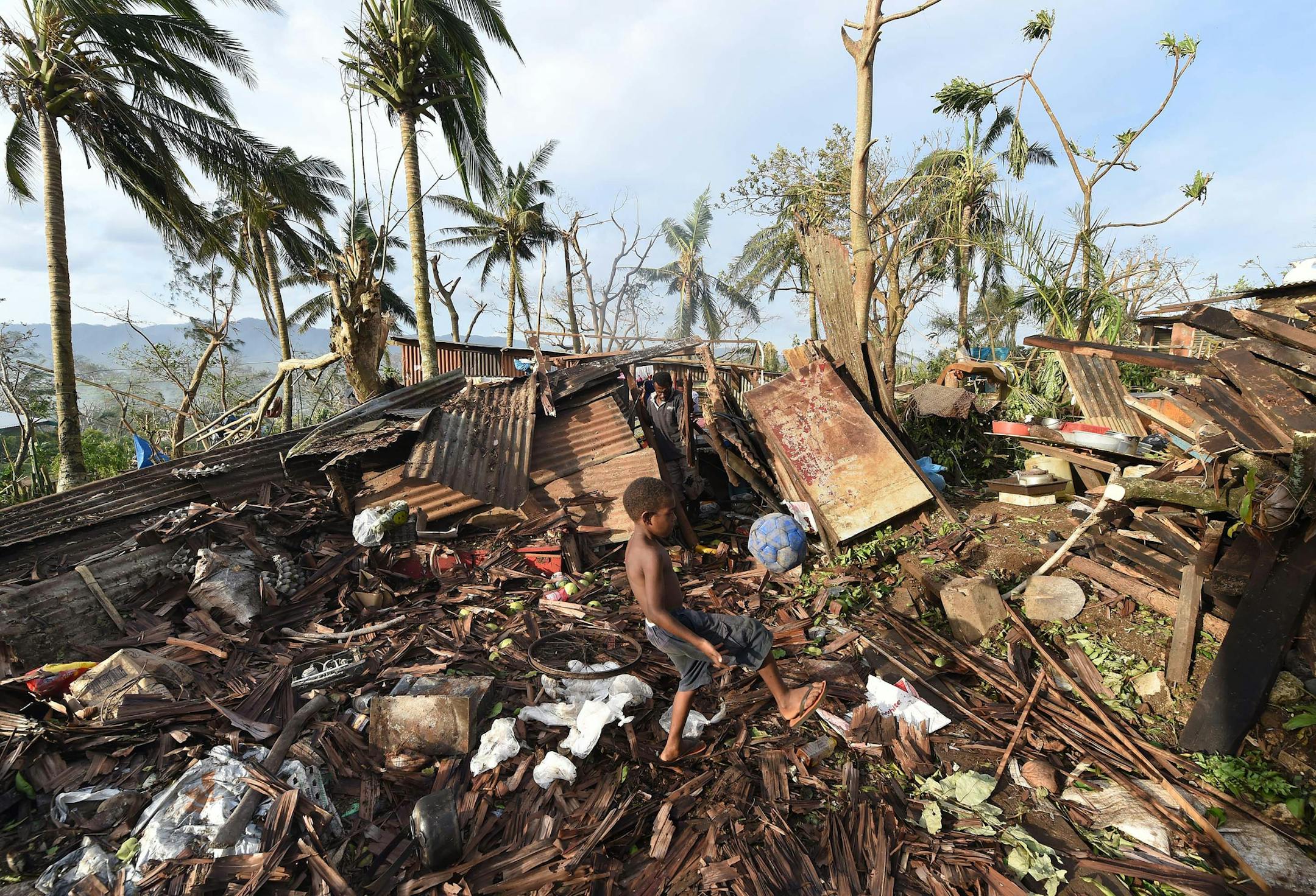 Samuel, only his first name given, kicks a ball through the ruins of their family home as his father, Phillip, at back, picks through the debris in Port Vila, Vanuatu in the aftermath of Cyclone Pam Monday, March 16, 2015. Vanuatu's President Baldwin Lonsdale said Monday that the cyclone that hammered the tiny South Pacific archipelago over the weekend was a "monster" that has destroyed or damaged 90 percent of the buildings in the capital and has forced the nation to start anew. (AP Photo/Dave