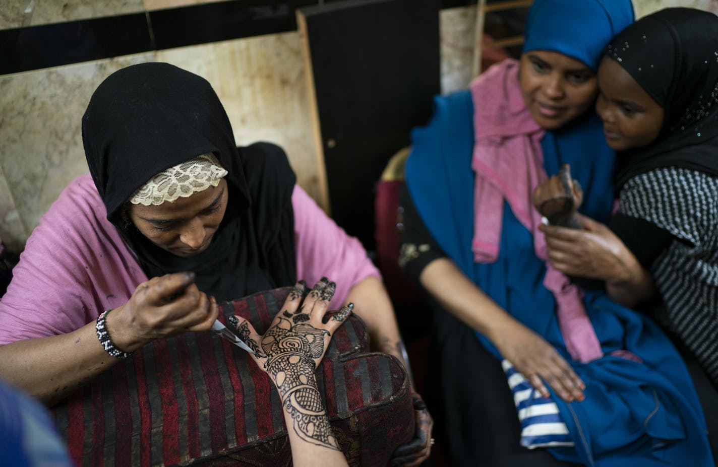 Farhiyo Ali drew a henna design on a customer as Fatima Hassan snuggled her daughter Hanna Hassan while waiting for her turn in preparation for Eid at Sihaam Henna at Karmel Mall in Minneapolis on Monday.