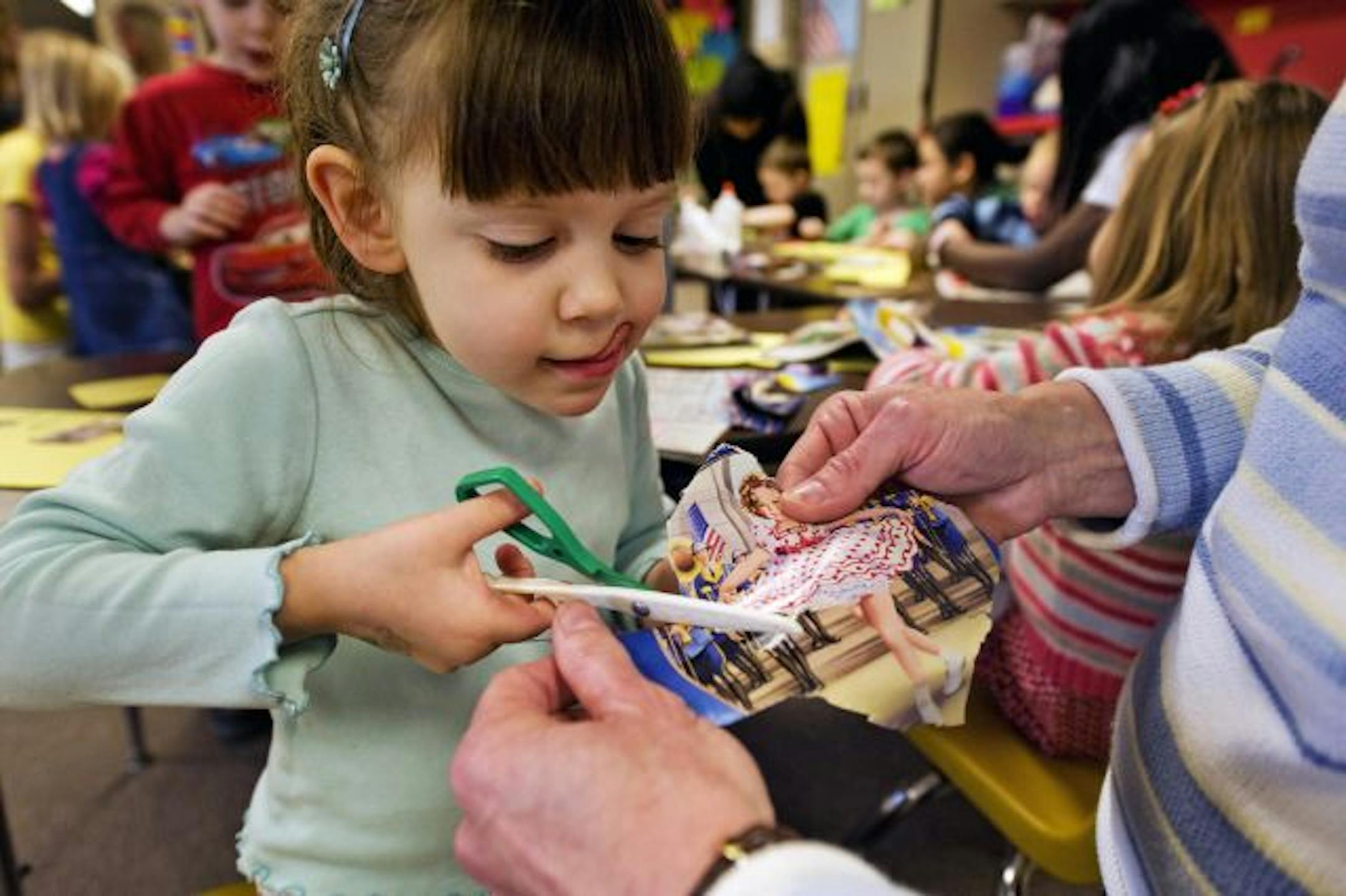 No running with these scissors: Four-year-old Maggie Nyhus concentrated on cutting out a picture from a magazine with the helping hands of Marlys Thom.